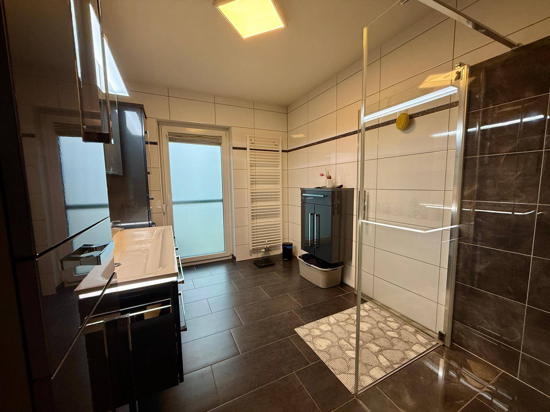 Modernes Badezimmer mit dunklen Fliesen, großer Duschkabine und weißem Waschbecken.