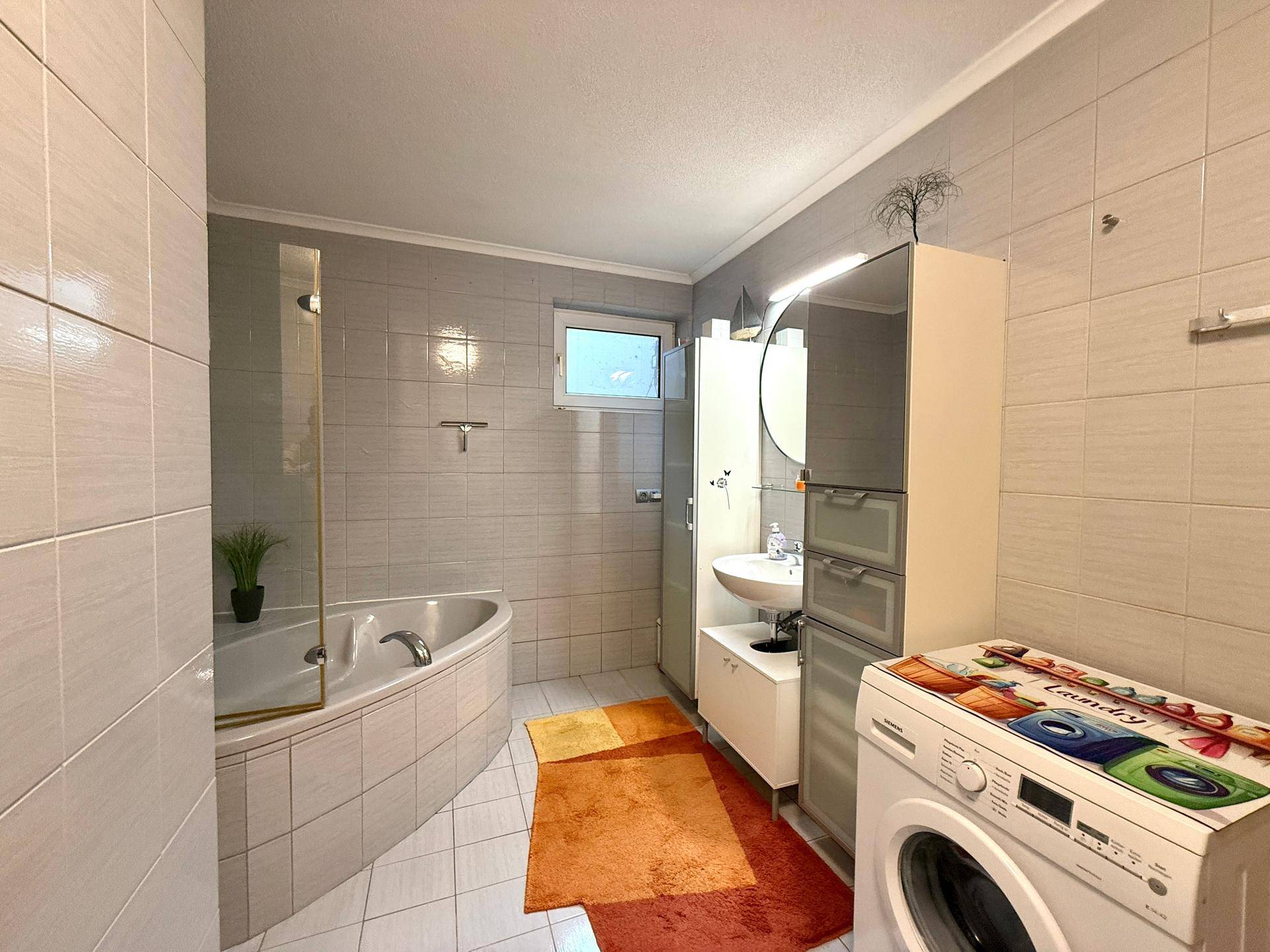 Badezimmer mit Badewanne, Dusche, Waschmaschine und Fenster für Tageslicht.