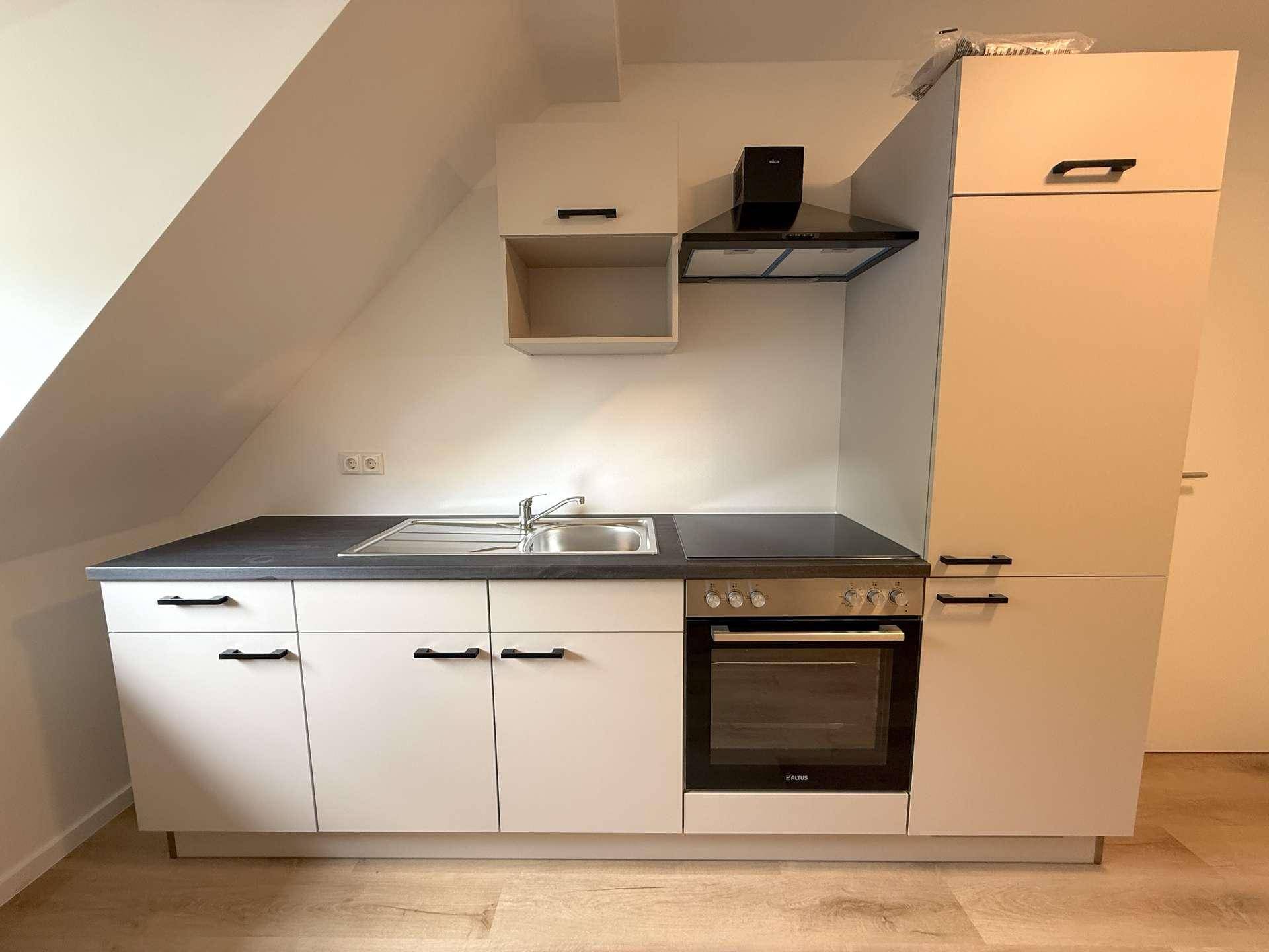 Moderne Küchenzeile mit weißen Schränken, integriertem Backofen und Dunstabzugshaube unter der Dachschräge.