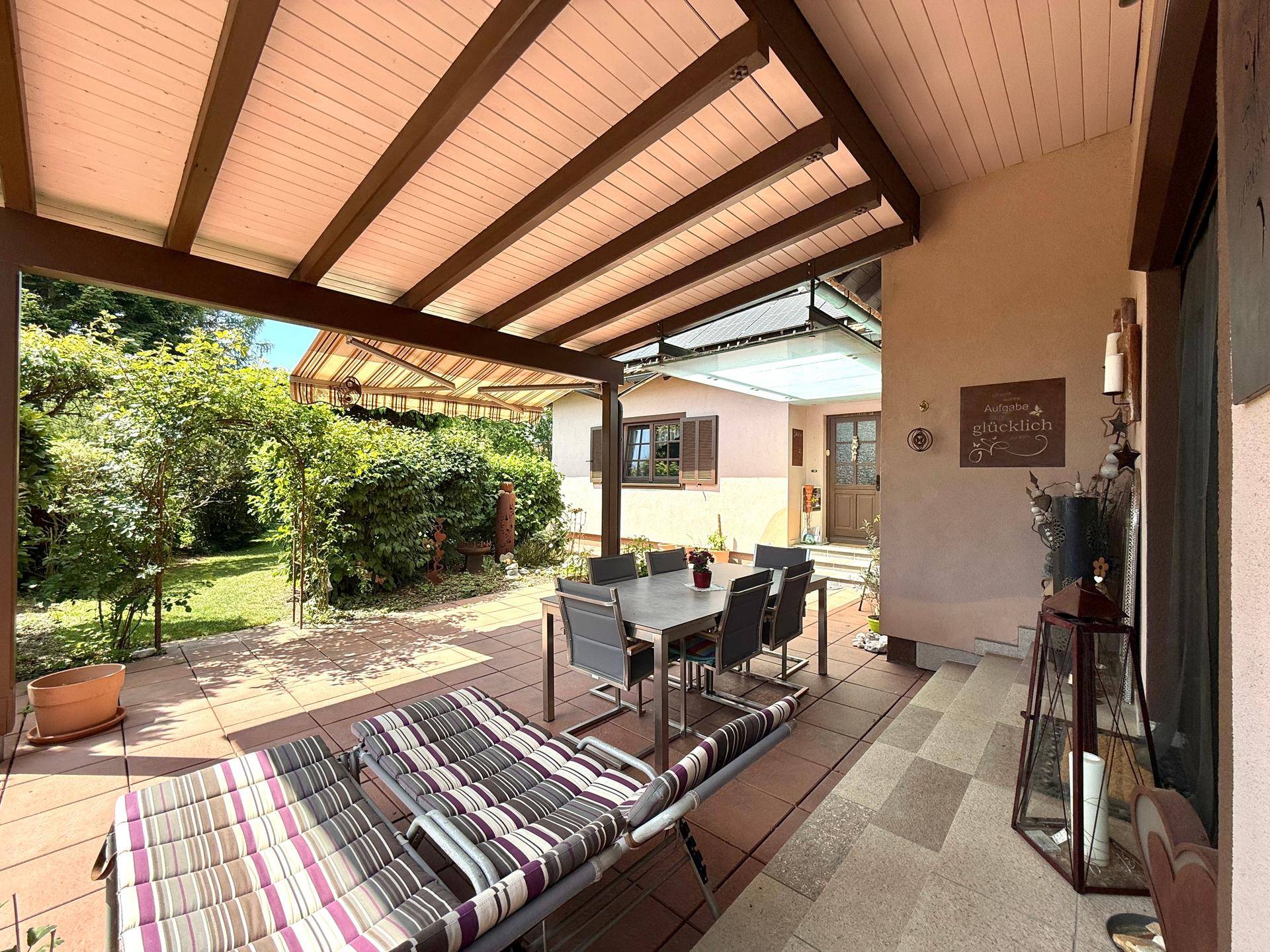Geräumige überdachte Terrasse mit Blick auf den gepflegten Garten und viel Grün.