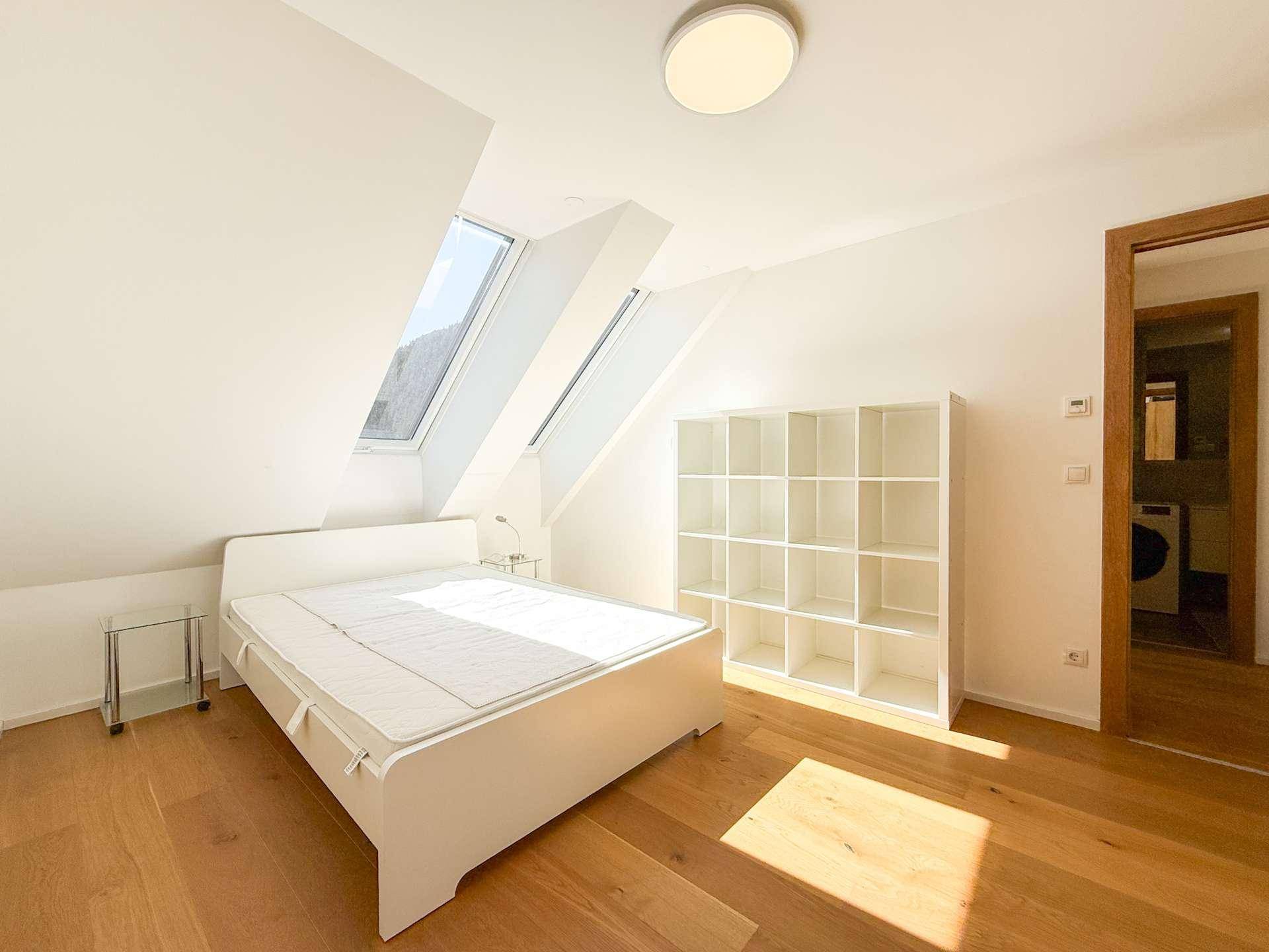 Geräumiges Schlafzimmer mit Holzboden, weißem Regal und zwei Dachfenstern für eine helle Atmosphäre.