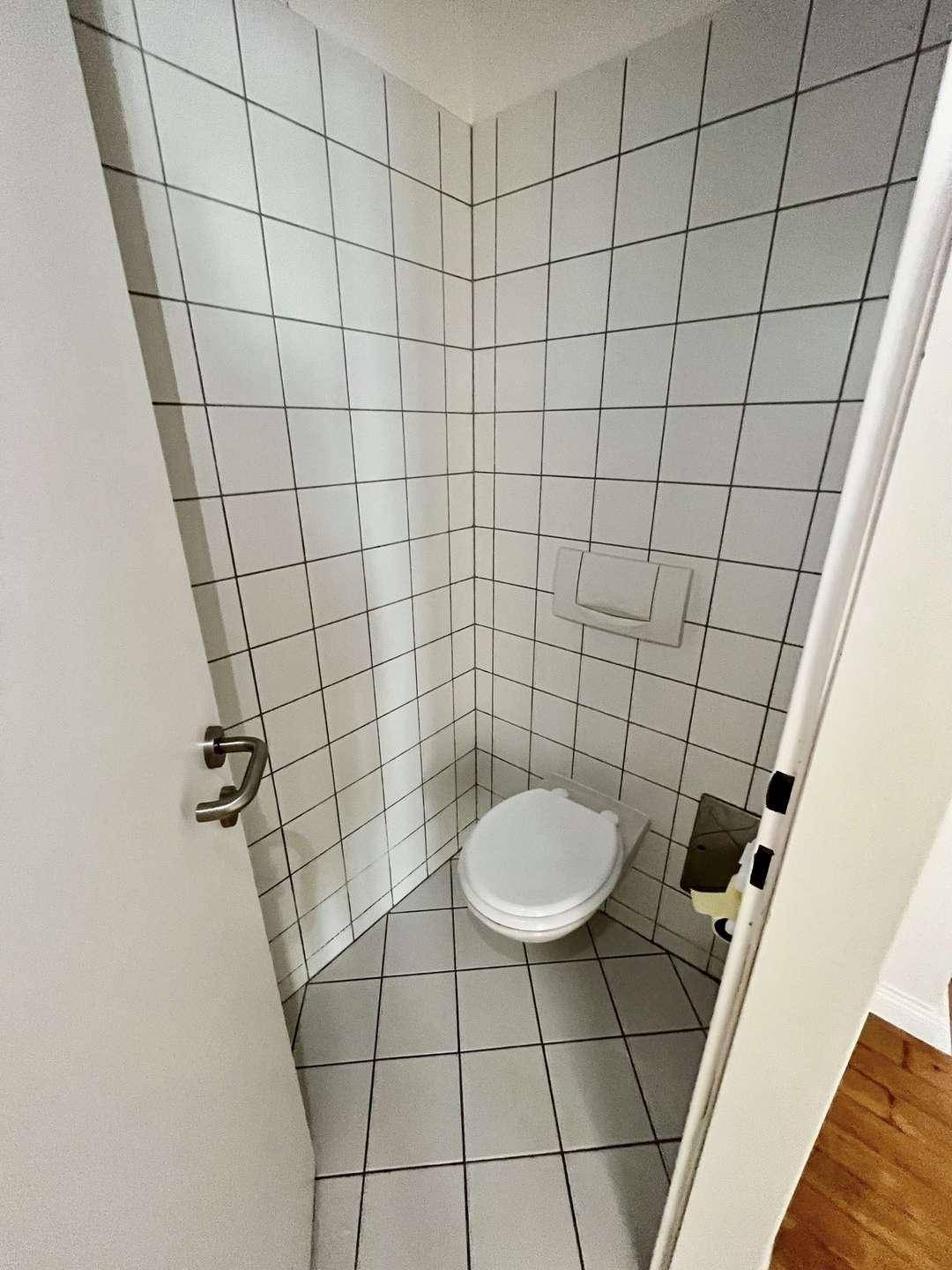 Separates WC mit Wand-WC und weißen Fliesen, platzsparend und praktisch gestaltet.