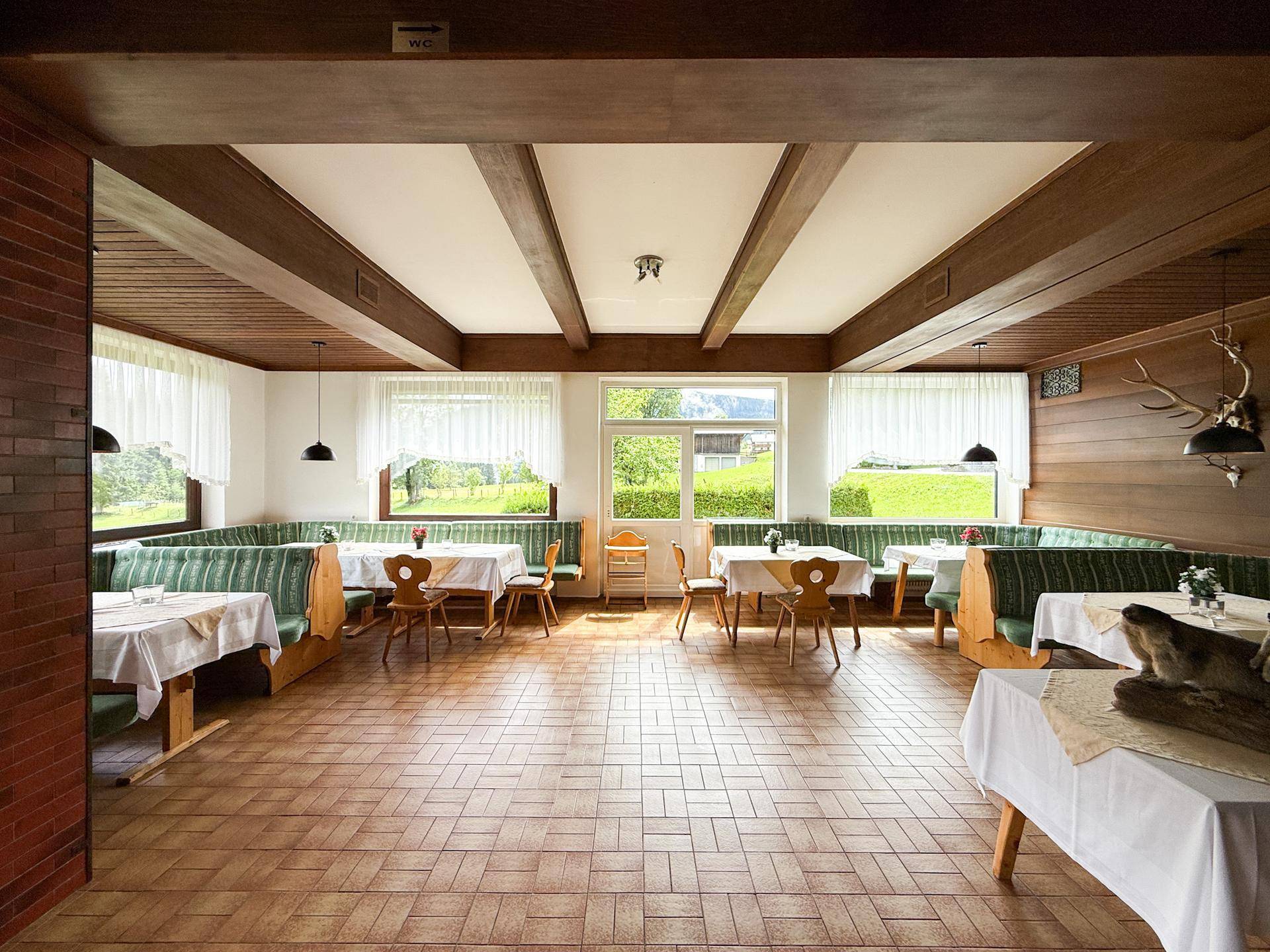 Traditioneller Speisesaal mit Holzbalken, gepolsterten Bänken und Blick auf die grüne Landschaft.