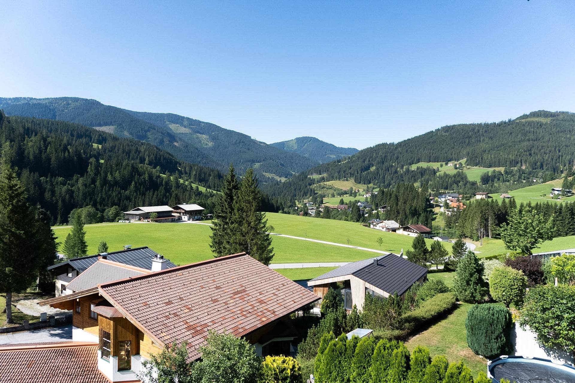 Weitläufiger Blick über grüne Hügel, Wälder und ein kleines Dorf in der Ferne.