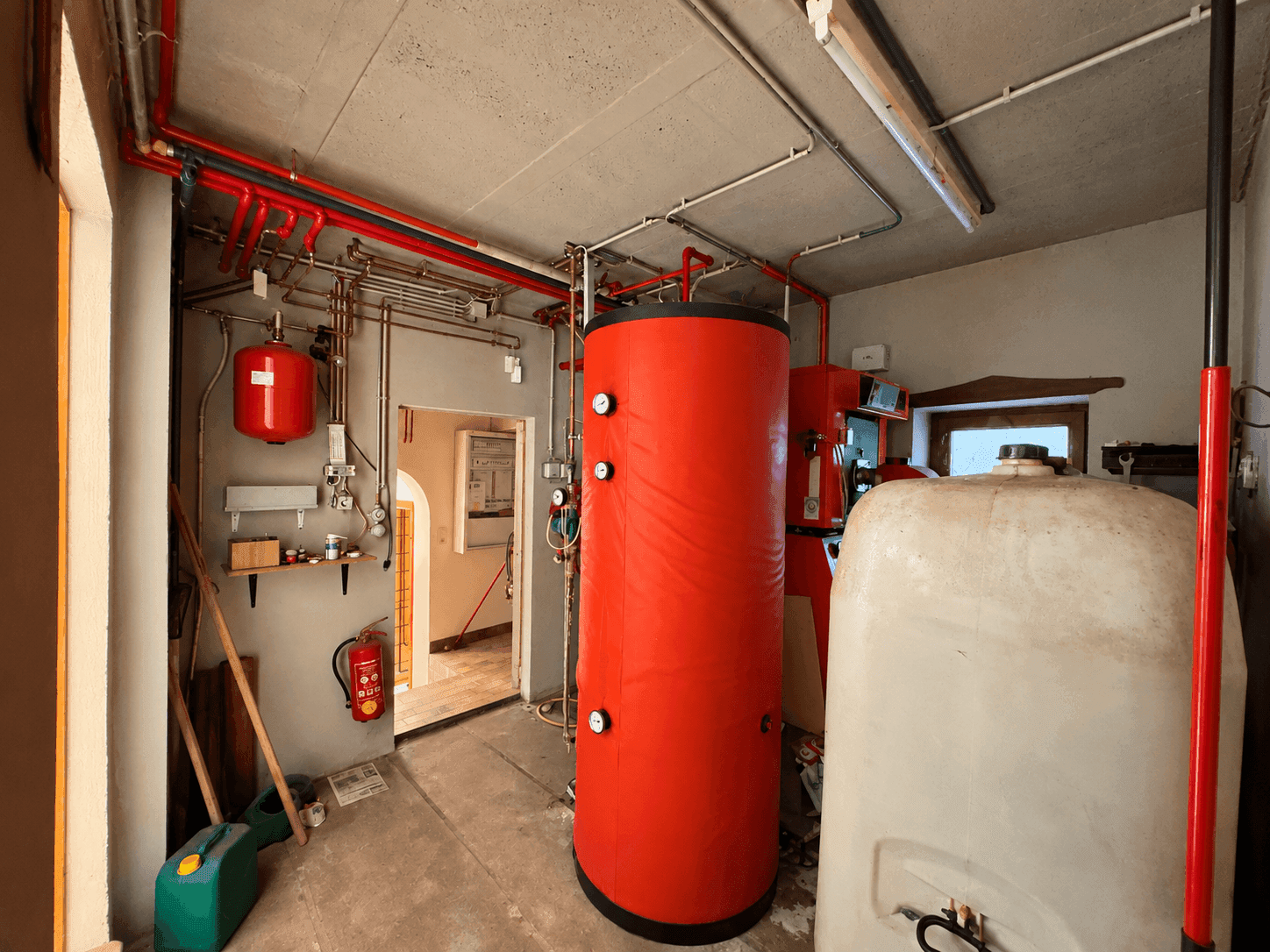 Heizungsraum mit Warmwasserspeicher, Rohren und technischer Ausstattung.
