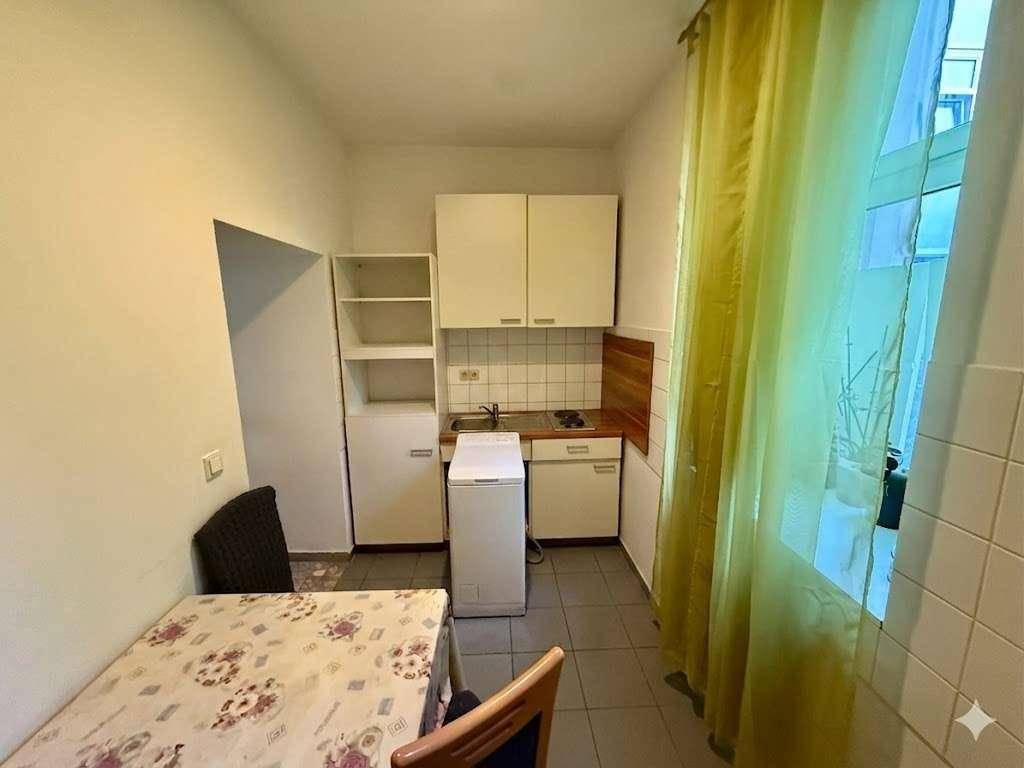 Kleine Küche mit weißen Oberschränken, Spüle und einem Esstisch am Fenster.
