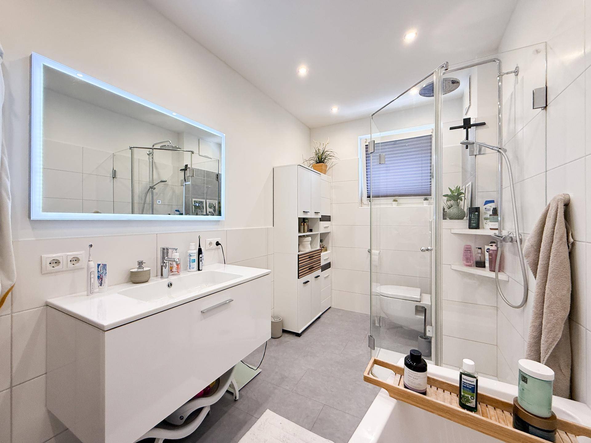 Modernes Badezimmer mit großer Dusche, Badewanne und beleuchtetem Spiegel.