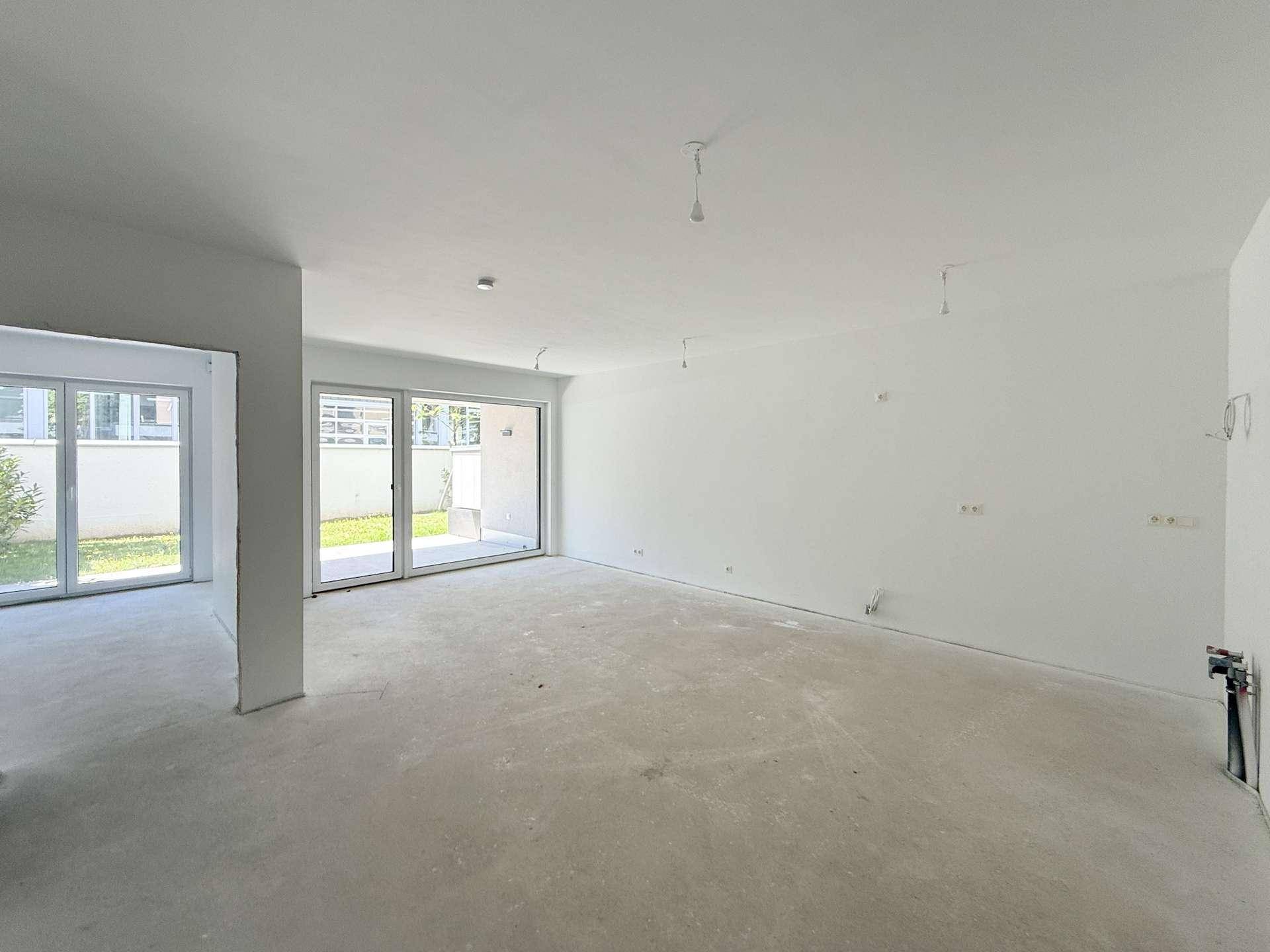 Leerer Wohnbereich im Rohbau mit großen Schiebetüren und Blick ins Grüne.