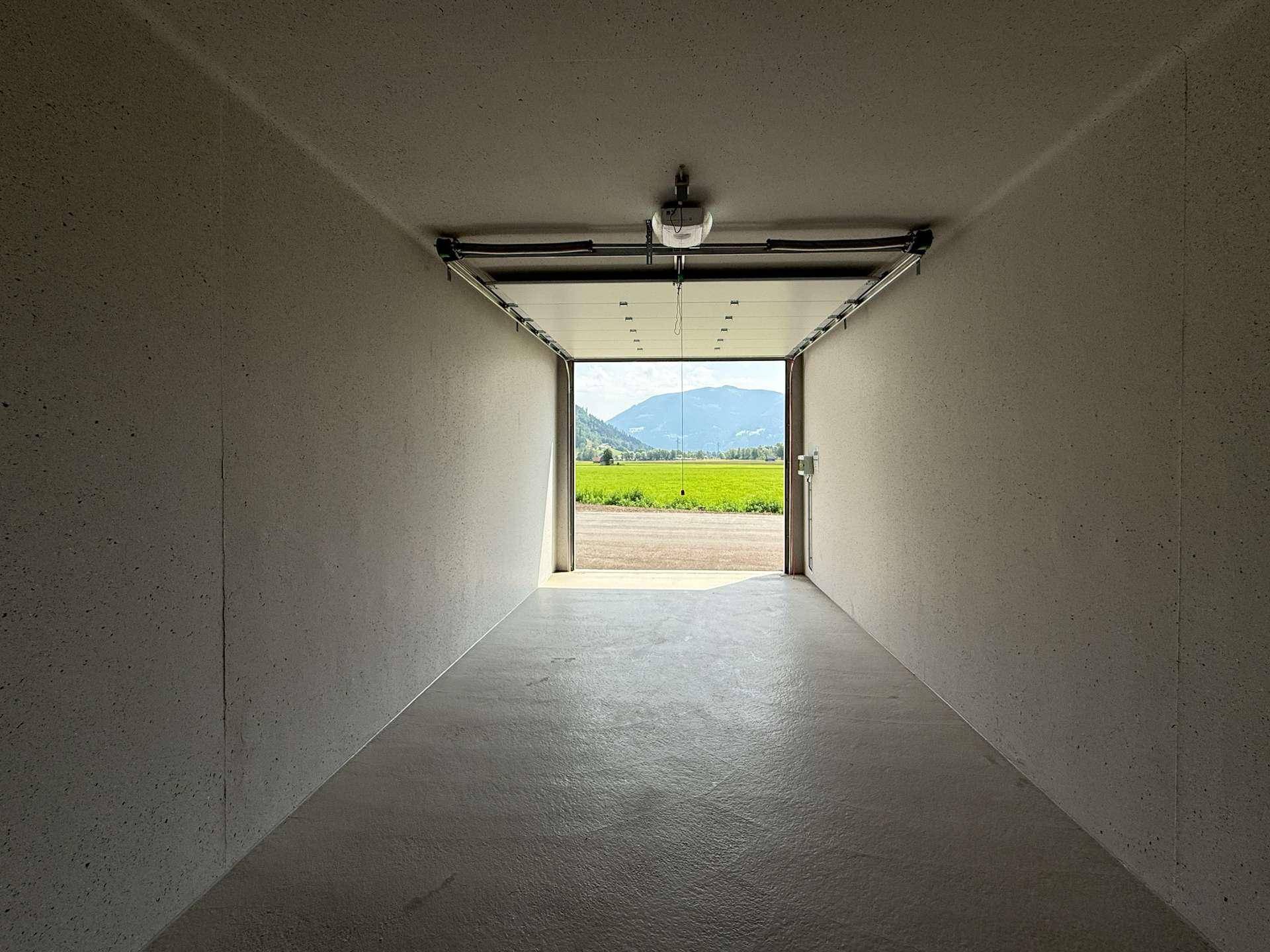 Geräumige Garagenbox mit Blick auf grüne Felder und Berge durch das offene Tor.