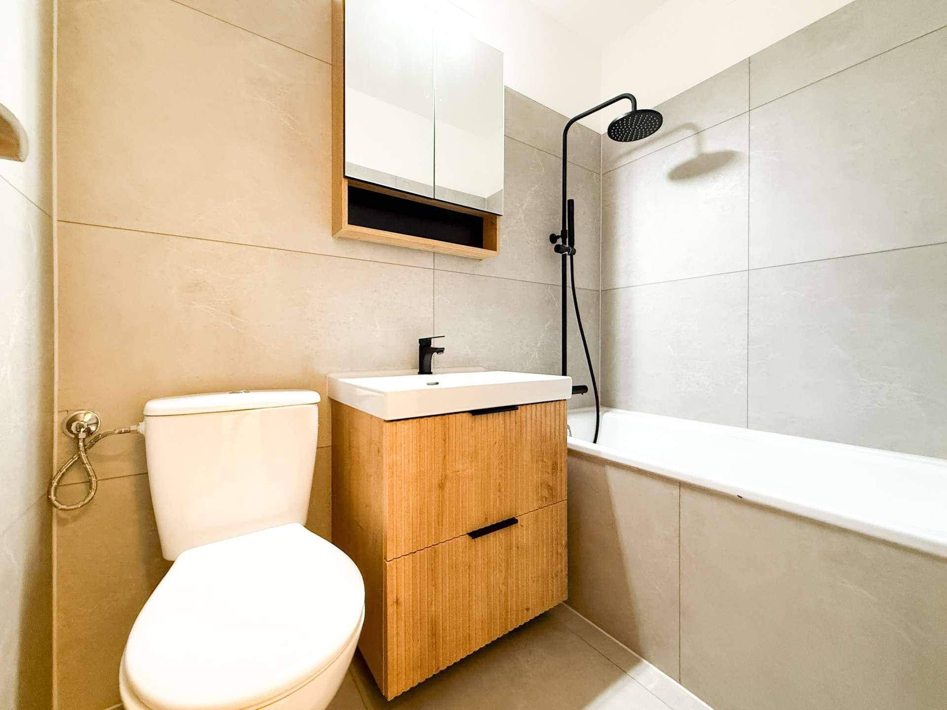 Modernes Badezimmer mit hellen Fliesen, Holzelementen und Badewanne mit Duschfunktion.