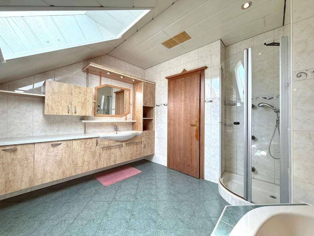 Geräumiges Badezimmer mit Waschtisch, Dusche und Dachfenster, hell gefliest.