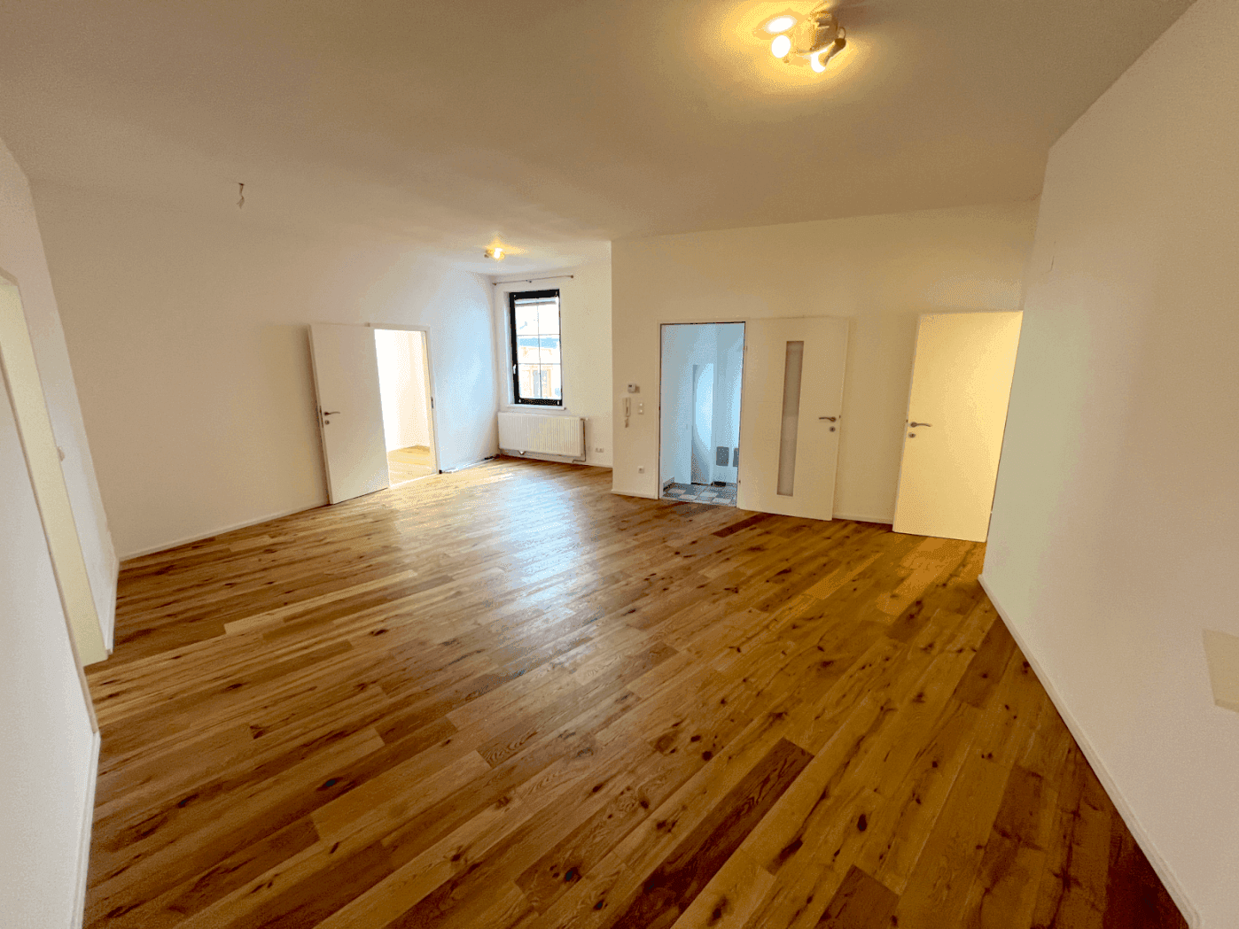 Geräumiges Wohnzimmer mit hellem Holzparkett und mehreren Türen, die zu anderen Räumen führen.