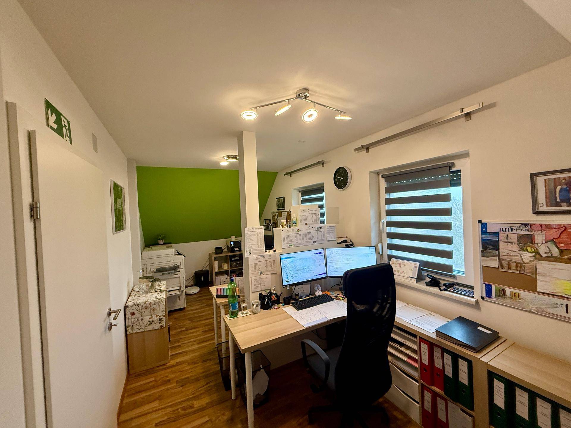 Helles Dachgeschoss-Büro mit Schreibtisch, zwei Monitoren und grüner Akzentwand.