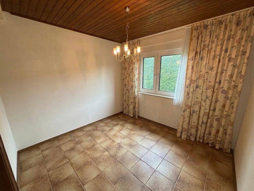 Leerer Raum mit Fliesenboden, Holztäfelung an der Decke und Fenster mit Vorhängen.
