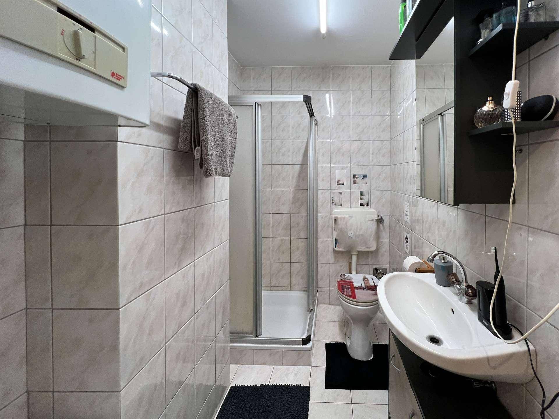 Gefliestes Badezimmer mit Duschkabine, WC und Waschbecken mit Unterschrank.