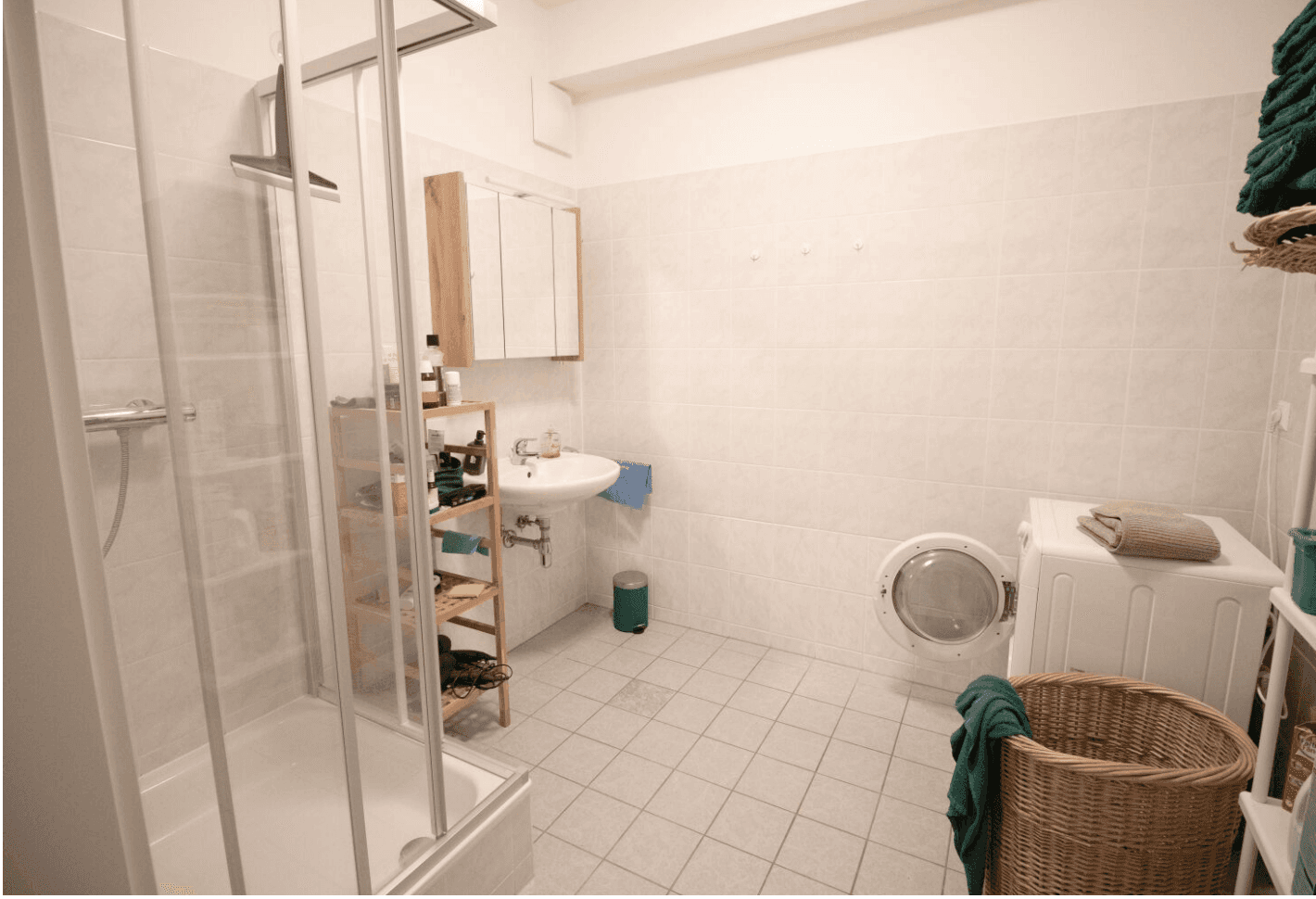 Helles Badezimmer mit Duschkabine, Waschbecken und praktischer Waschmaschine.