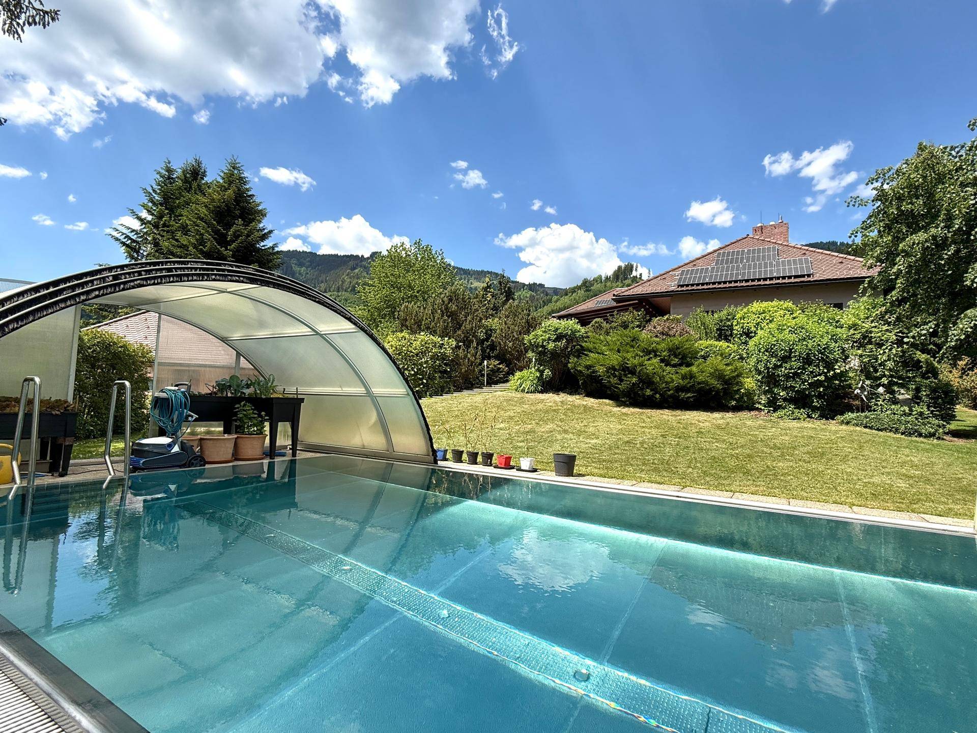Überdachter Swimmingpool im Garten mit Blick auf das Haus und die umliegende Landschaft.