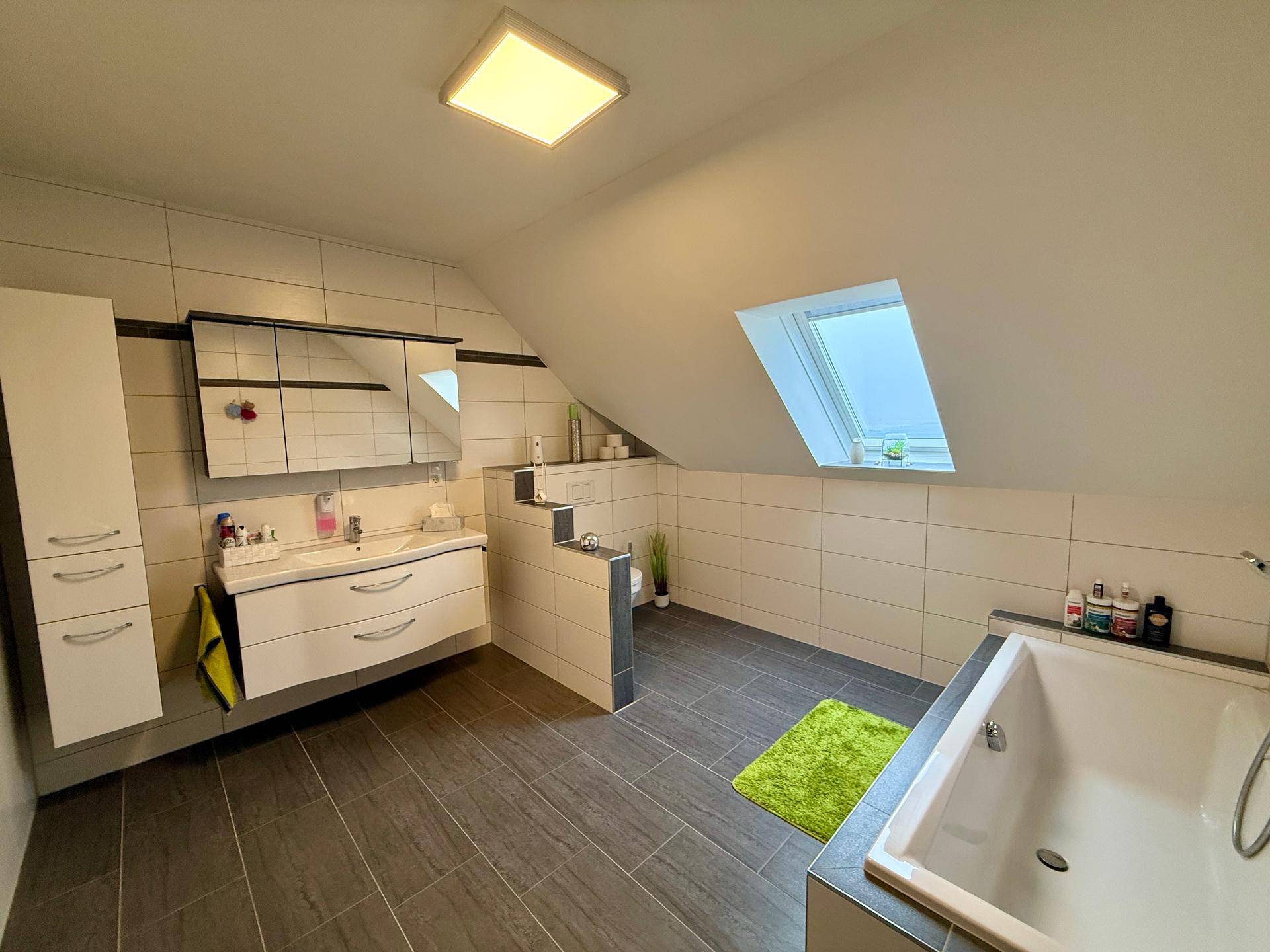 Modernes Badezimmer im Dachgeschoss mit Badewanne, Waschbecken und Dachfenster.