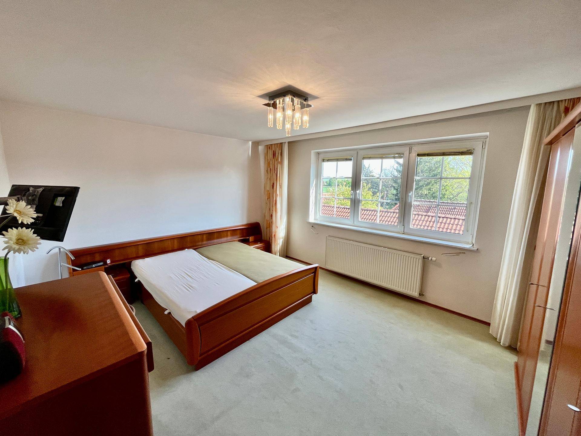 Helles Schlafzimmer mit Doppelbett, Teppichboden und großem Fenster mit Ausblick.