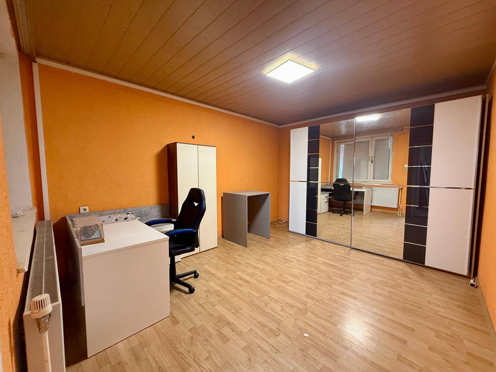 Schlafzimmer mit orangefarbenen Wänden, Holzboden und großem Spiegelschrank.