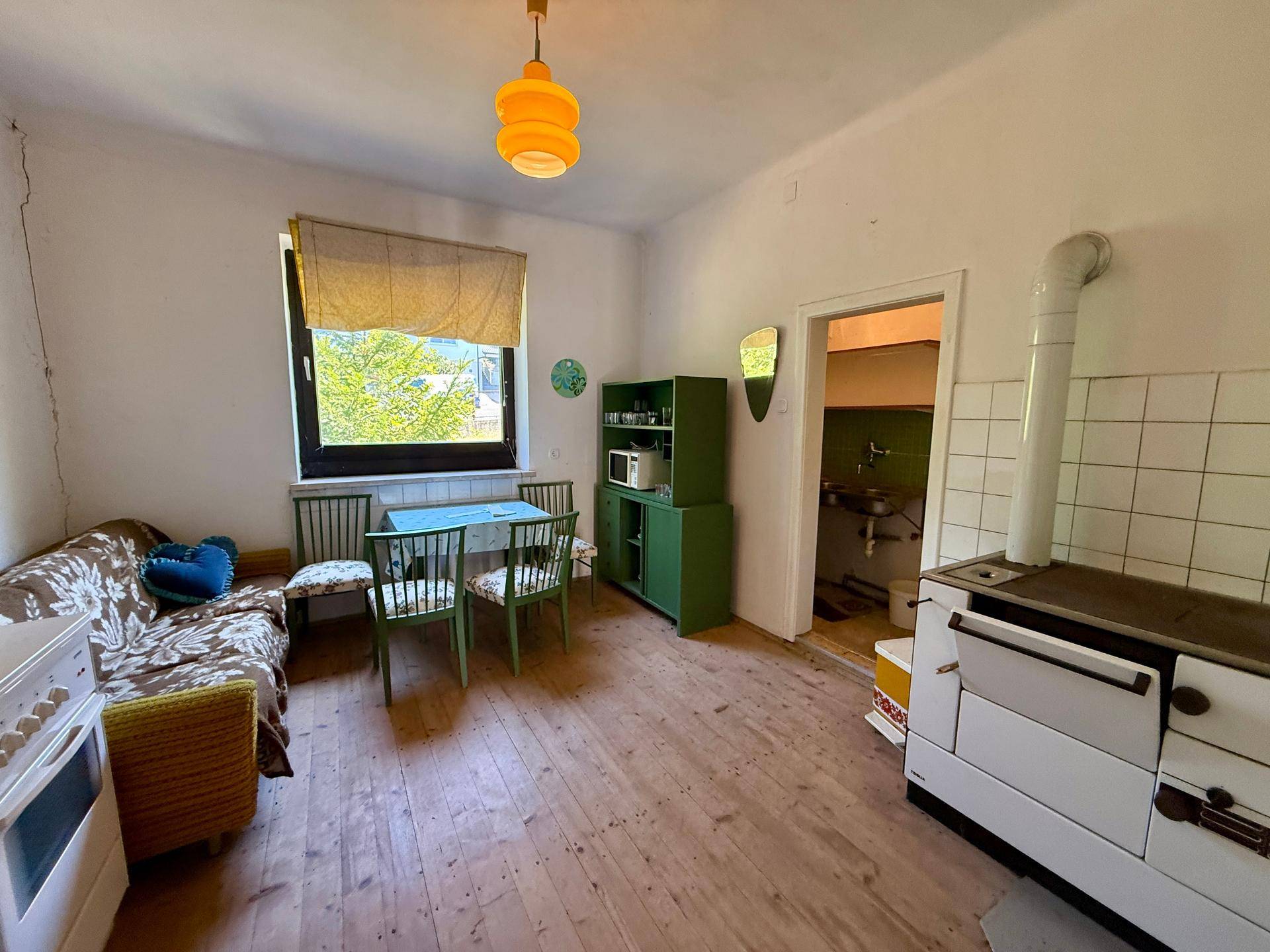 Geräumige Wohnküche mit Holzofen, Esstisch und Sofa, ideal für gemütliche Mahlzeiten.