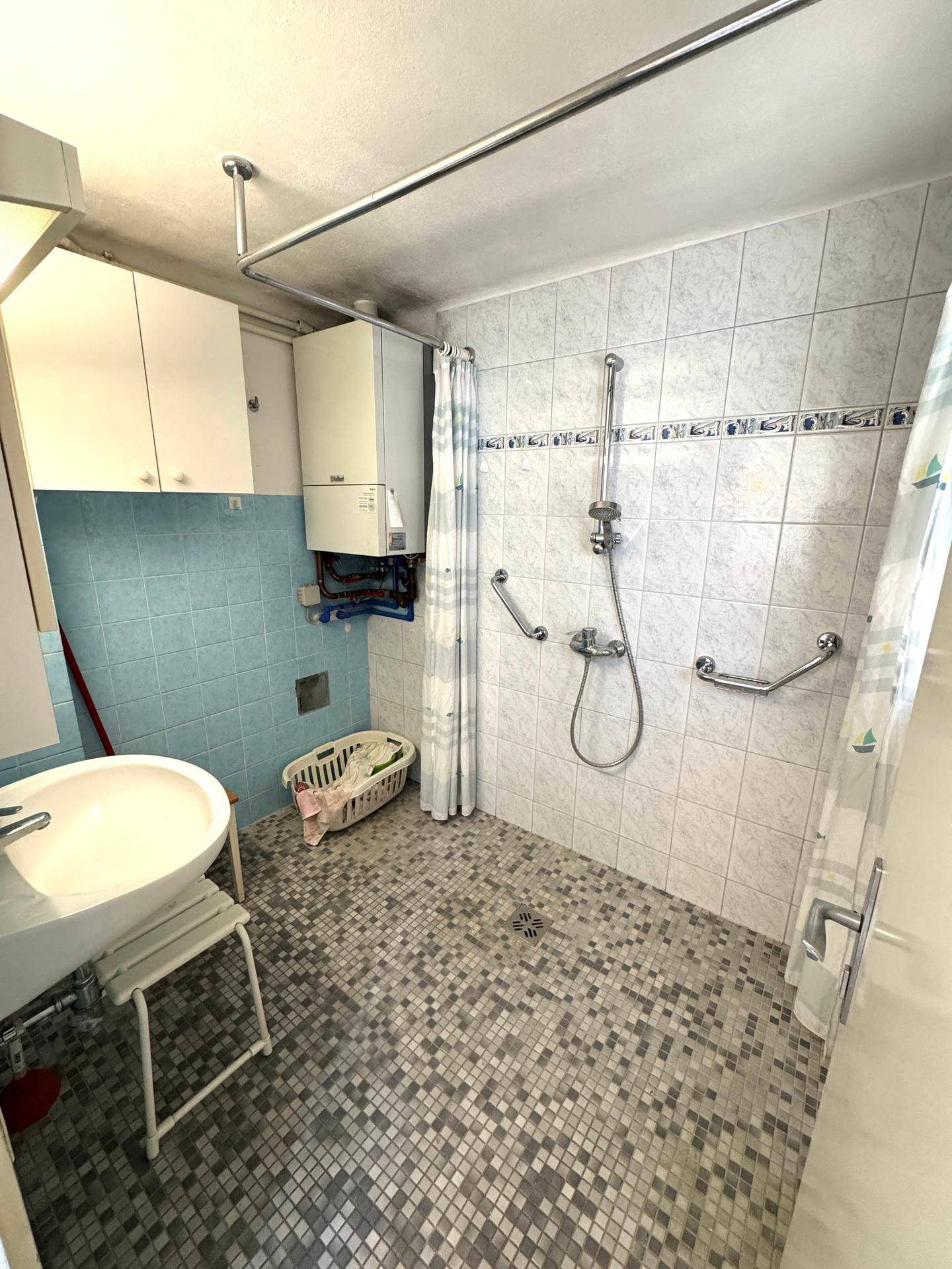 Badezimmer mit ebenerdiger Dusche, Fliesenboden und Haltegriffen für Barrierefreiheit.