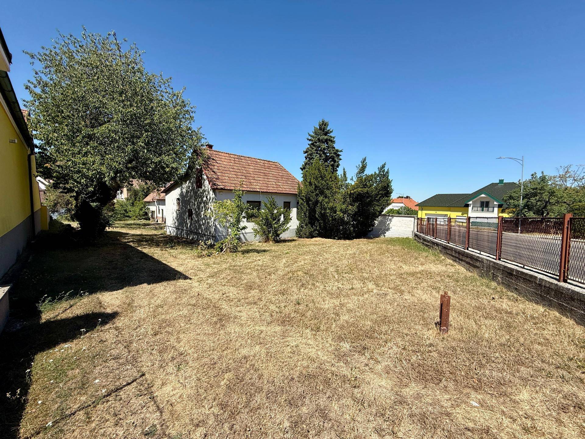 Weitläufiges Grundstück mit Rasenfläche und einem kleinen Haus im Hintergrund unter blauem Himmel.