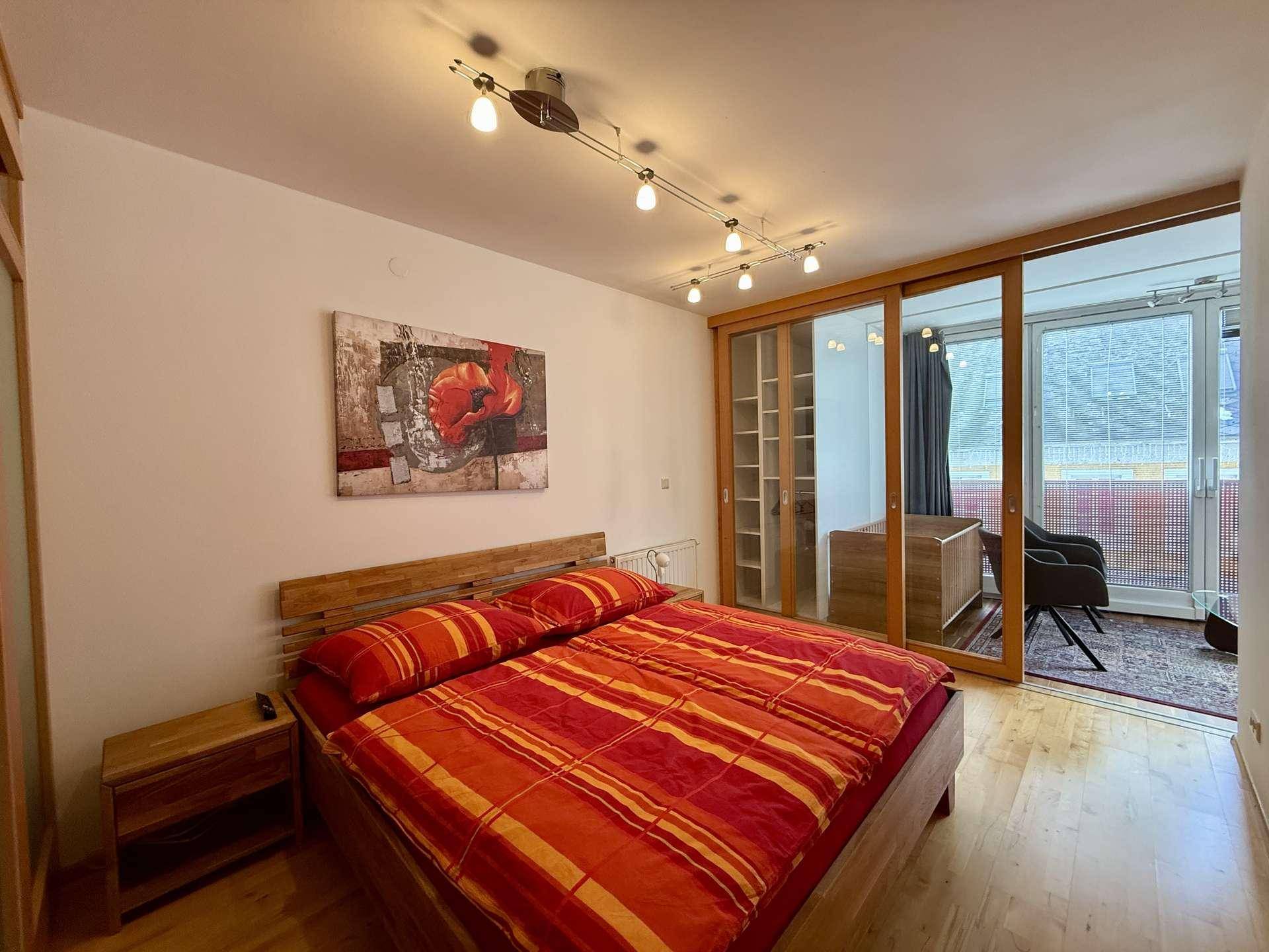 Gemütliches Schlafzimmer mit Doppelbett, Holzboden und Zugang zu einem verglasten Balkon.