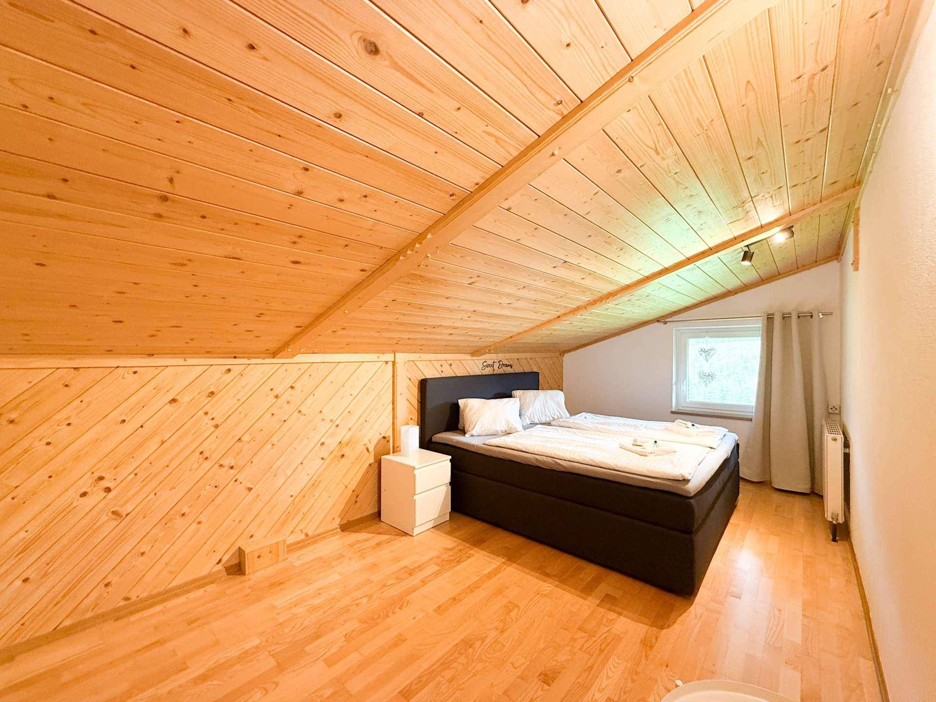 Gemütliches Schlafzimmer im Dachgeschoss mit Holzverkleidung, Doppelbett und Dachschräge.