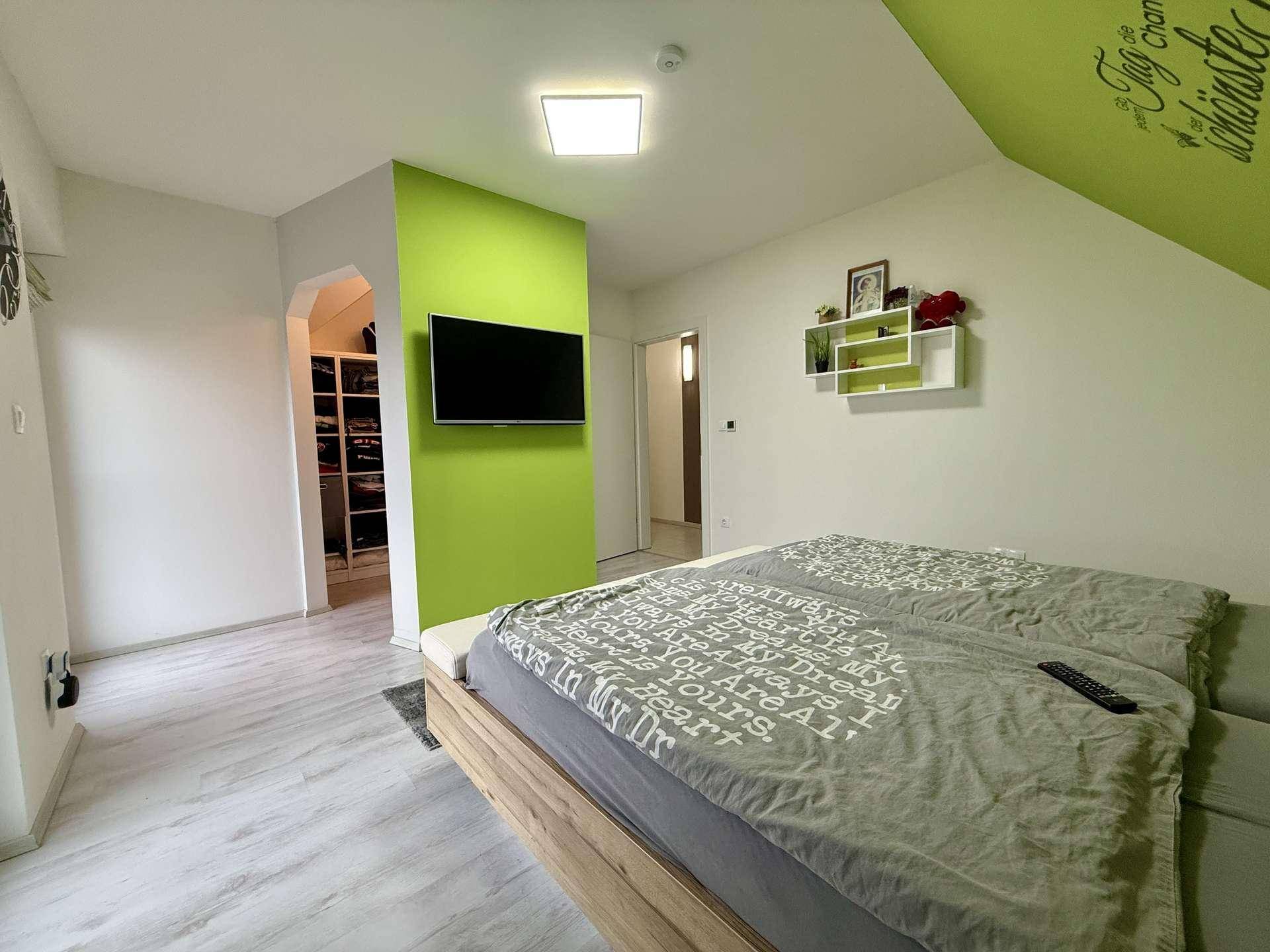 Modernes Schlafzimmer mit grüner Wand, Doppelbett und offenem Zugang zu einem begehbaren Kleiderschrank.