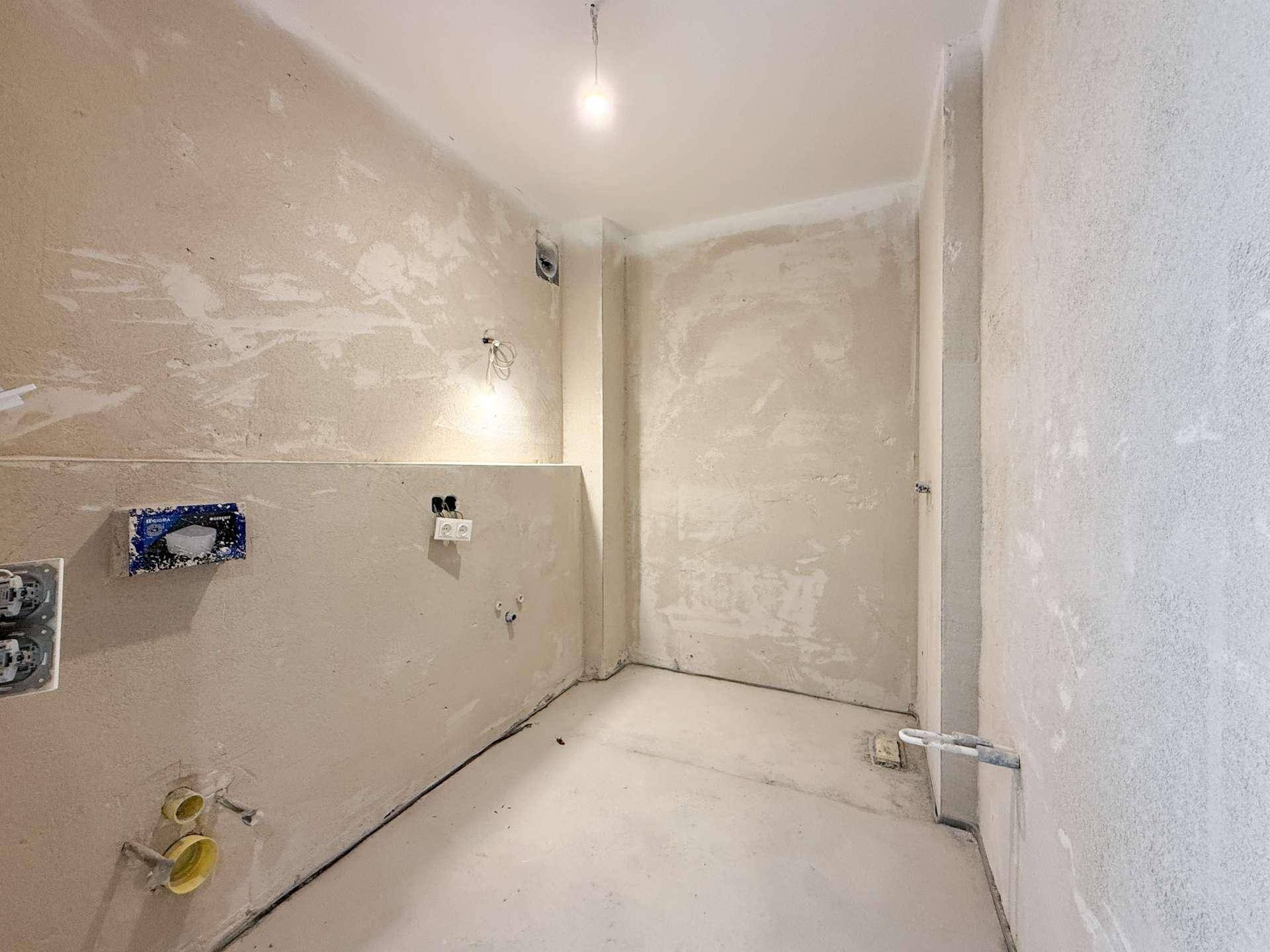 Rohbau-Badezimmer mit vorbereiteten Anschlüssen für Toilette und Waschbecken.