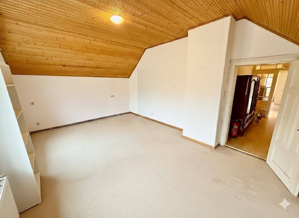 Leeres Zimmer mit Holzdecke und Teppichboden, ideal für ein Schlafzimmer oder Büro.