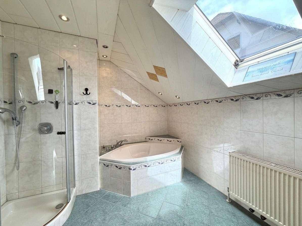 Helles Badezimmer mit Eckbadewanne, Dusche und Dachfenster unter der Dachschräge.