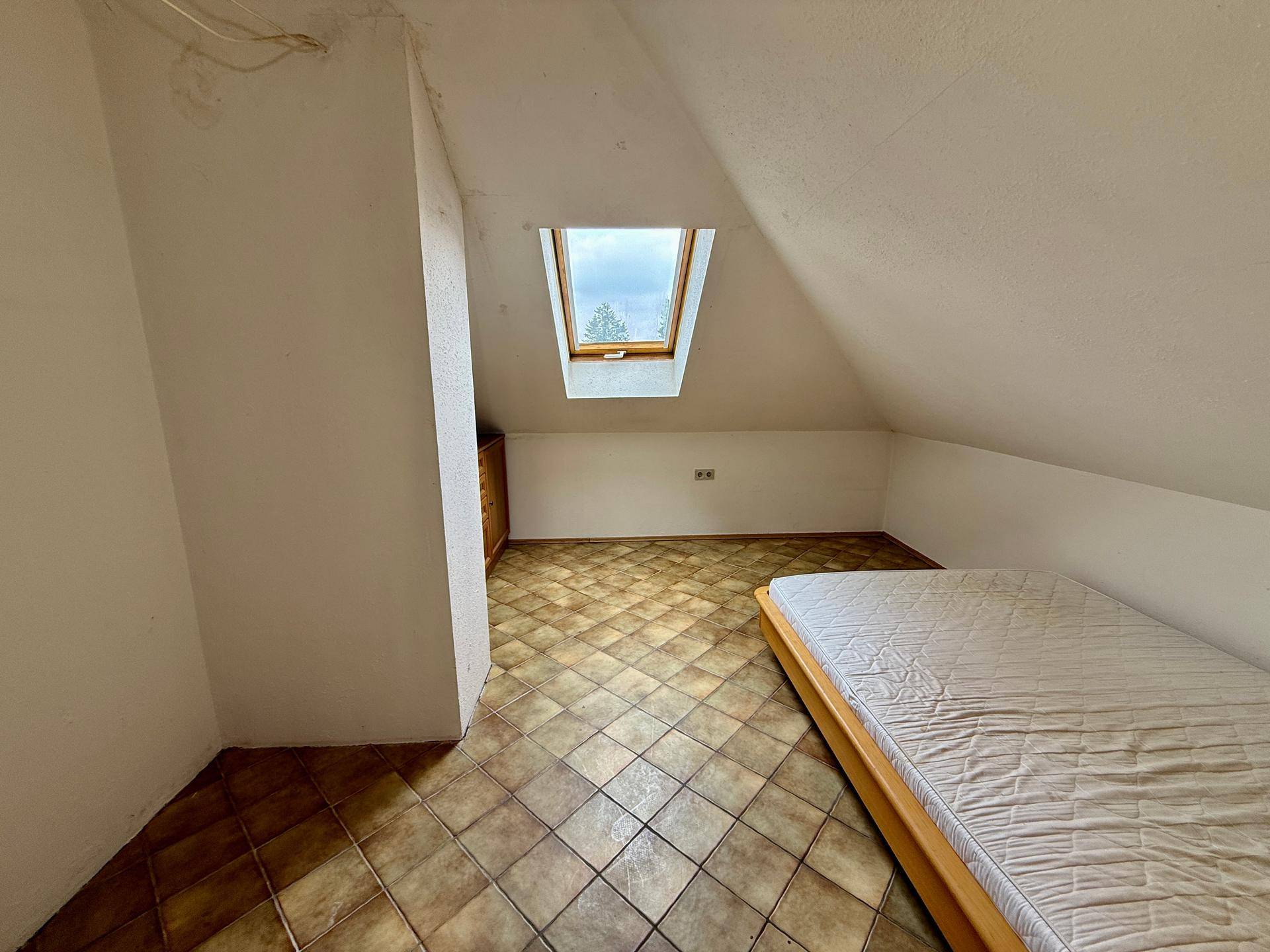 Helles Schlafzimmer im Dachgeschoss mit Dachfenster und Fliesenboden.