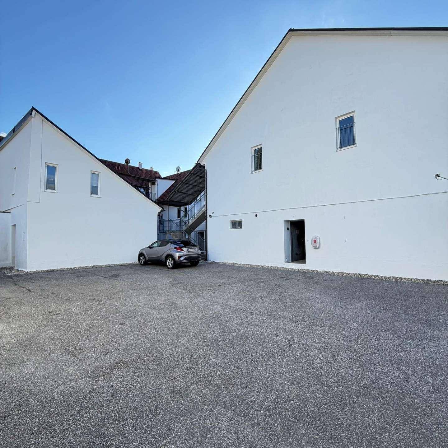 Außenansicht eines modernen Gebäudes mit weißer Fassade und einem Parkplatz davor unter blauem Himmel.