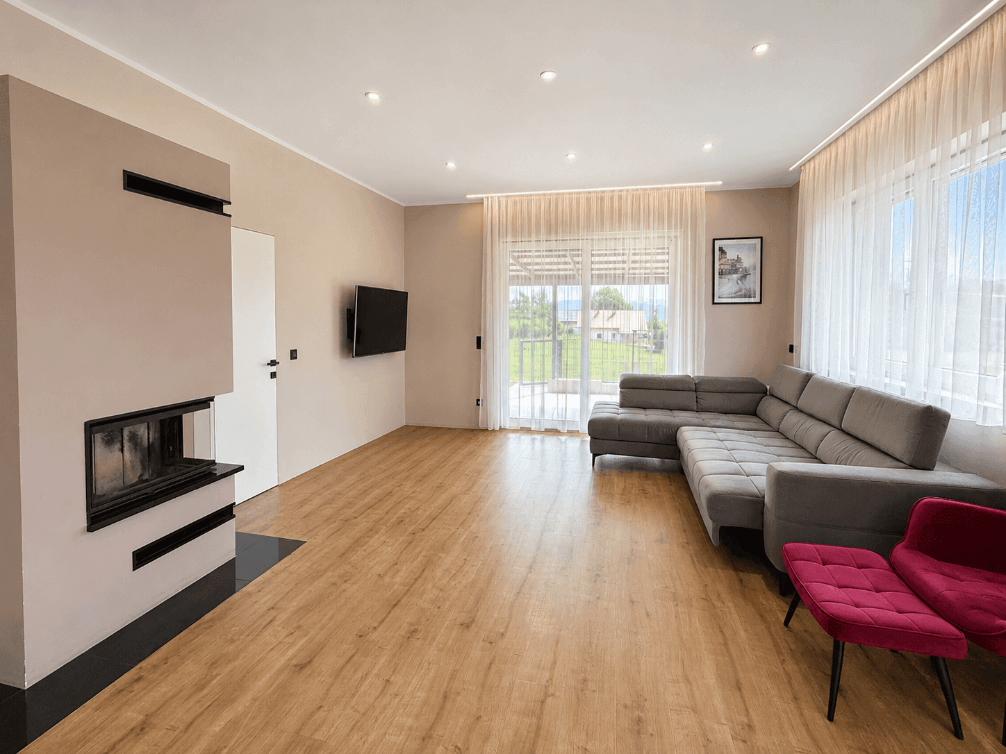 Helles Wohnzimmer mit modernem Kamin, Holzboden und Zugang zur Terrasse mit Weitblick.
