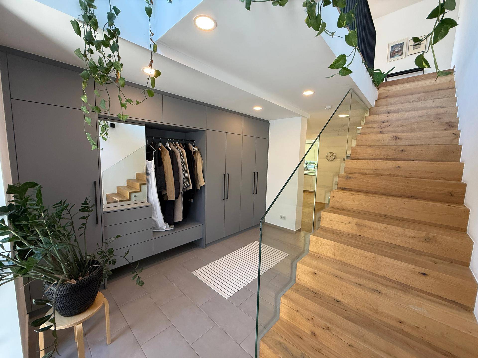 Heller Eingangsbereich mit modernen Einbauschränken, Holztreppe und Glasgeländer.