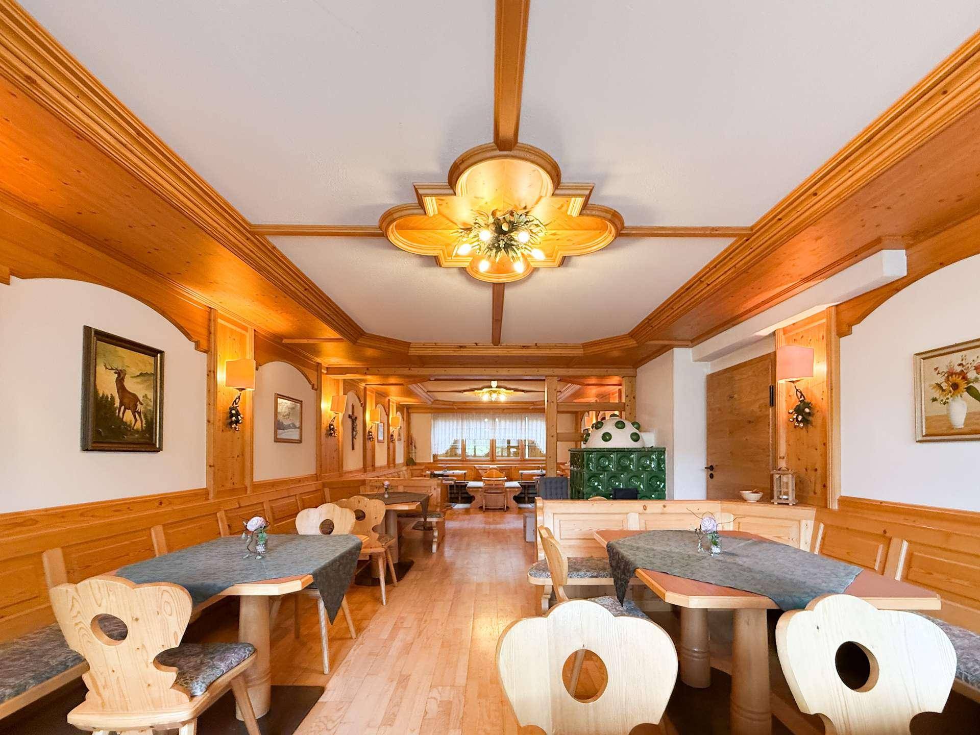 Traditioneller Speisesaal mit holzgetäfelten Wänden, Holztischen und einem Kachelofen.