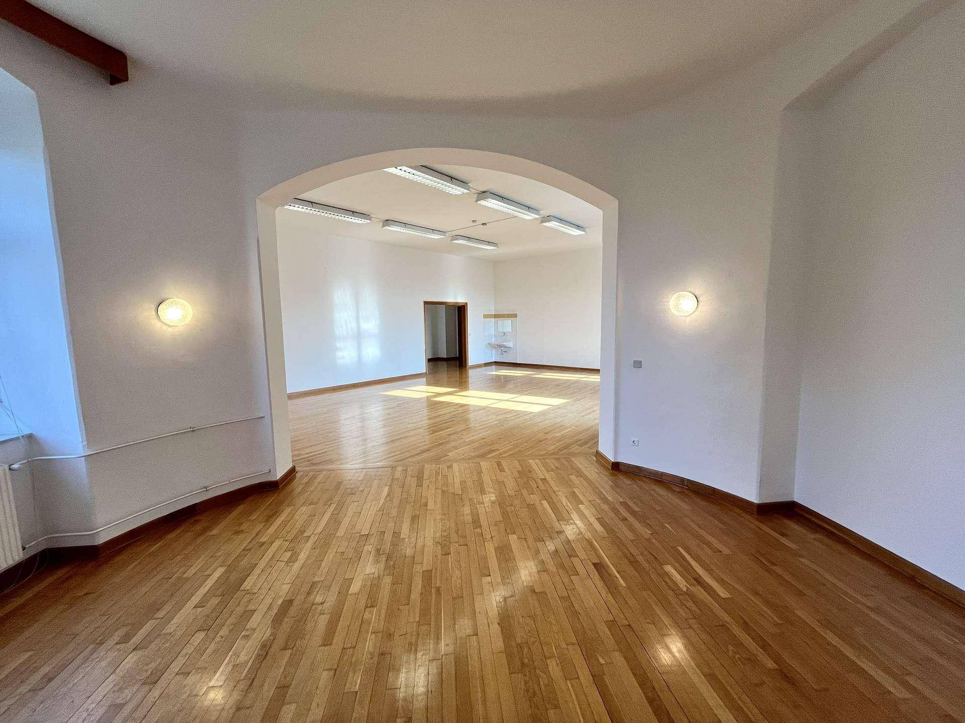 Heller Büroraum mit Holzboden und einem großen Bogen, der zu einem weiteren Bereich führt.