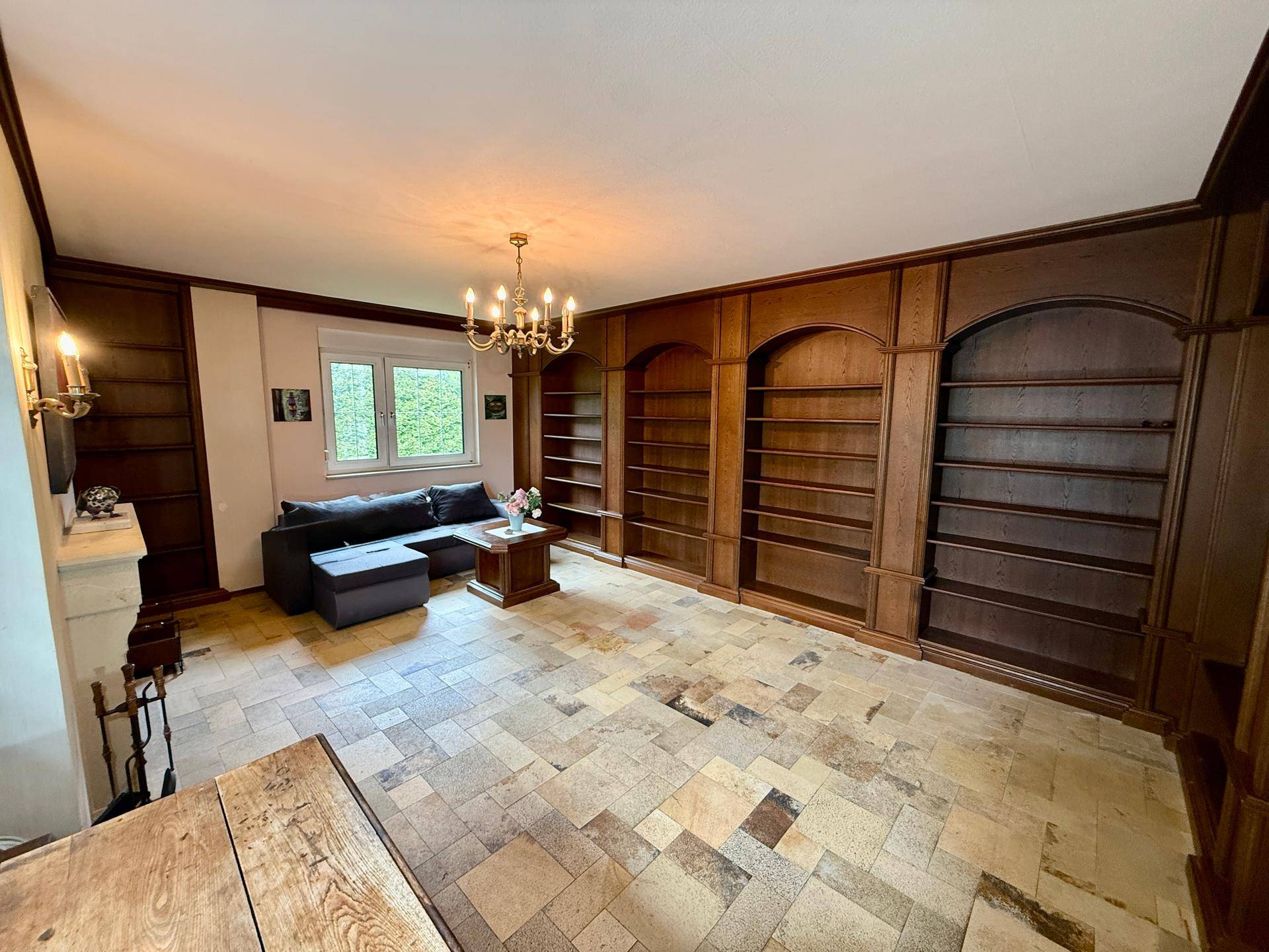 Wohnzimmer mit Holzwänden, integrierten Regalen und Blick ins Grüne durch das Fenster.