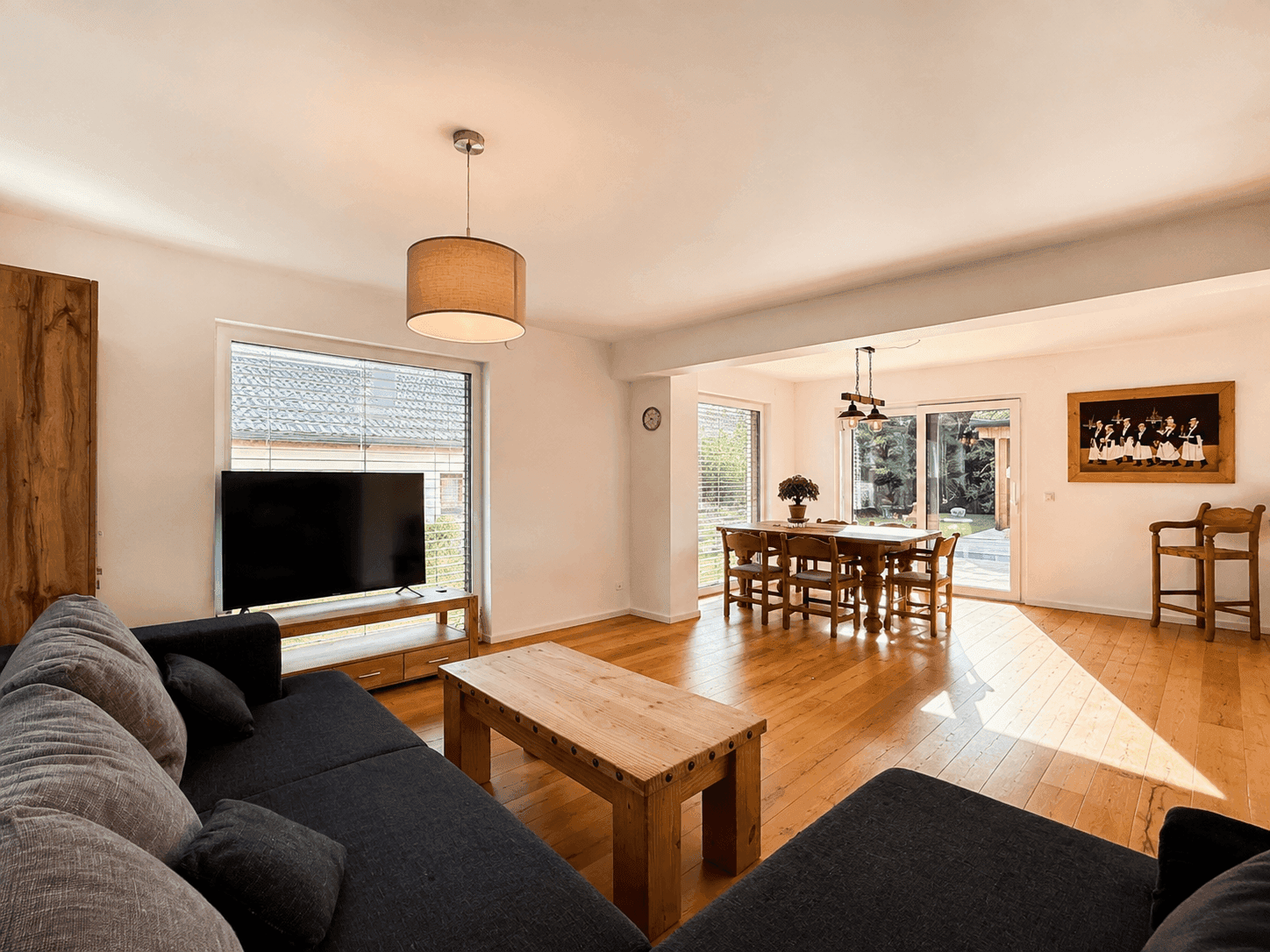 Helles Wohn-Esszimmer mit Holzboden, großem Sofa und traditionellem Esstisch.