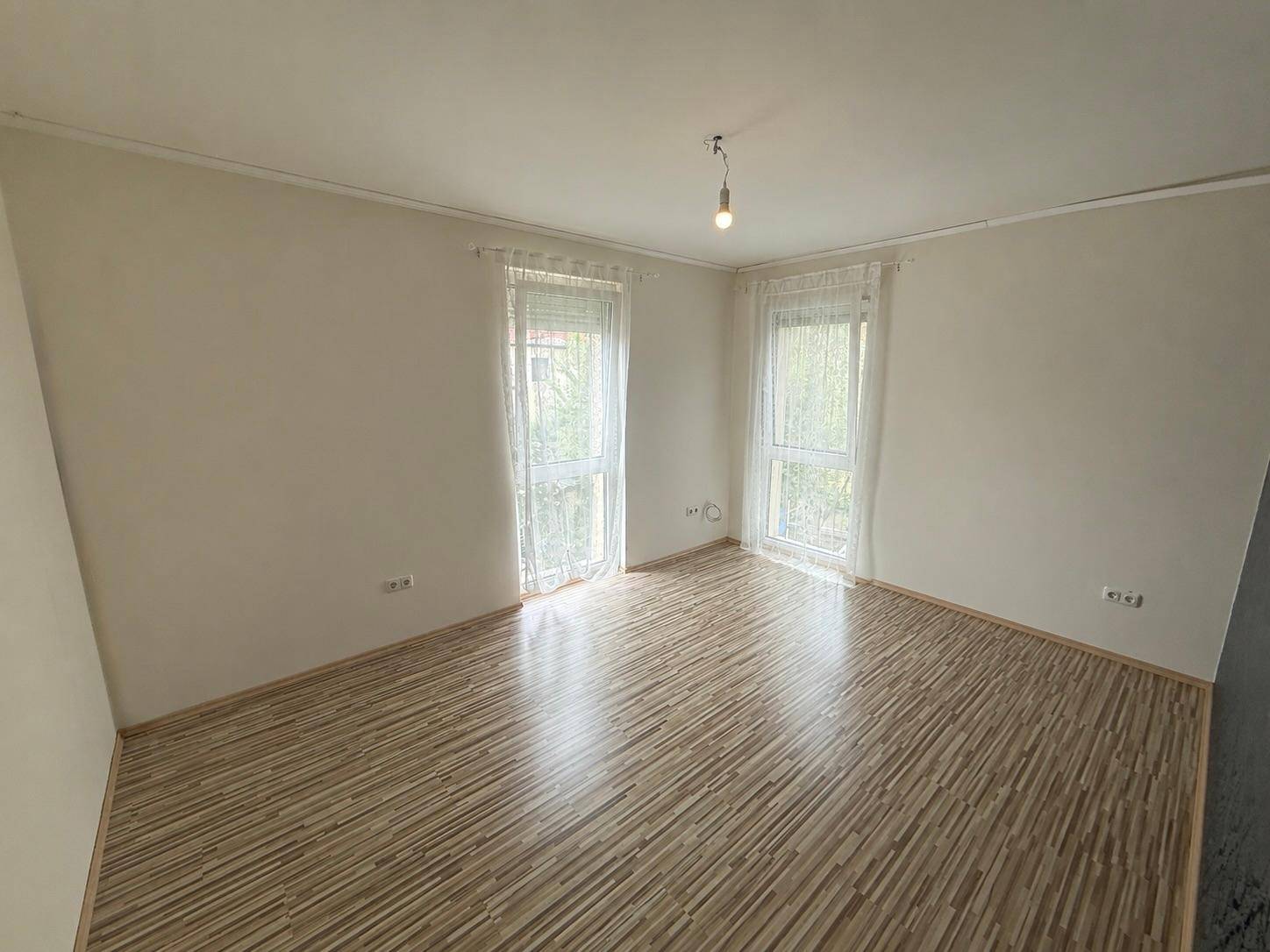 Helles Zimmer mit Laminatboden und zwei Fenstern, ideal als Schlaf- oder Kinderzimmer.