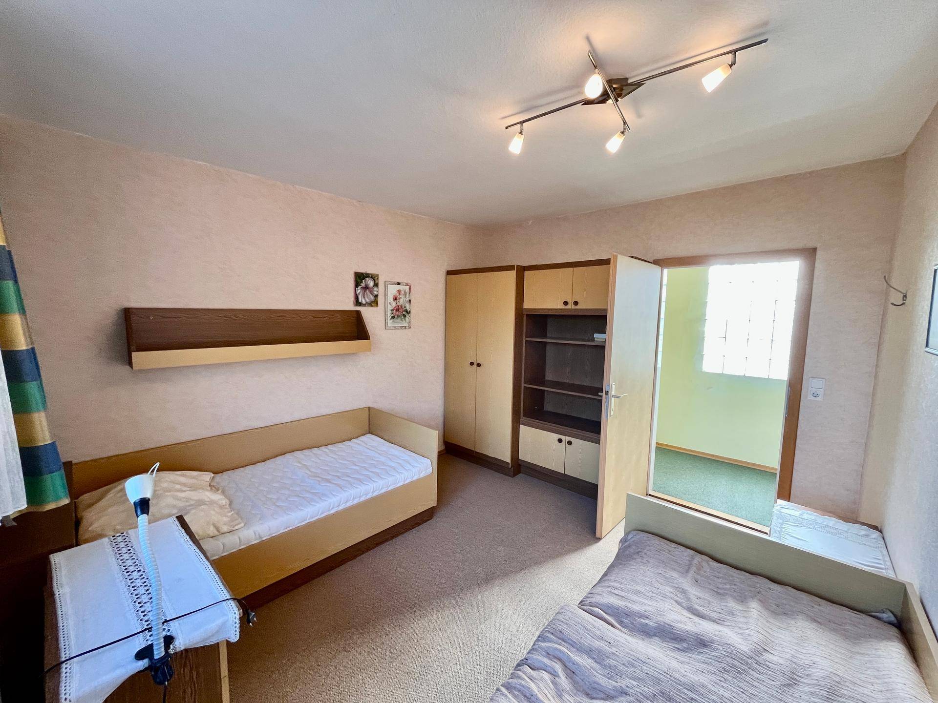 Schlafzimmer mit zwei Einzelbetten, Teppichboden und Zugang zu einem Nebenraum.