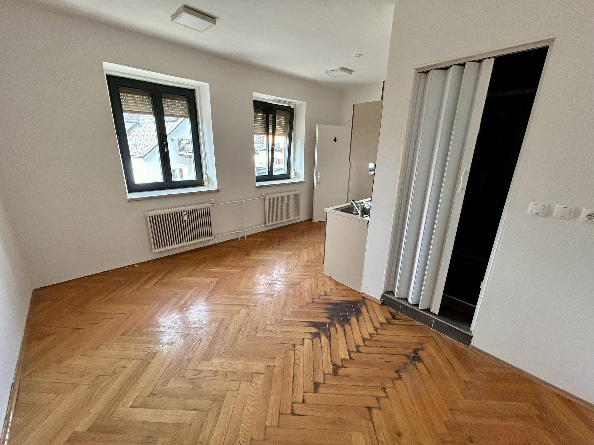 Heller Raum mit Fischgrätparkett, dunklen Fensterrahmen und Blick nach draußen.