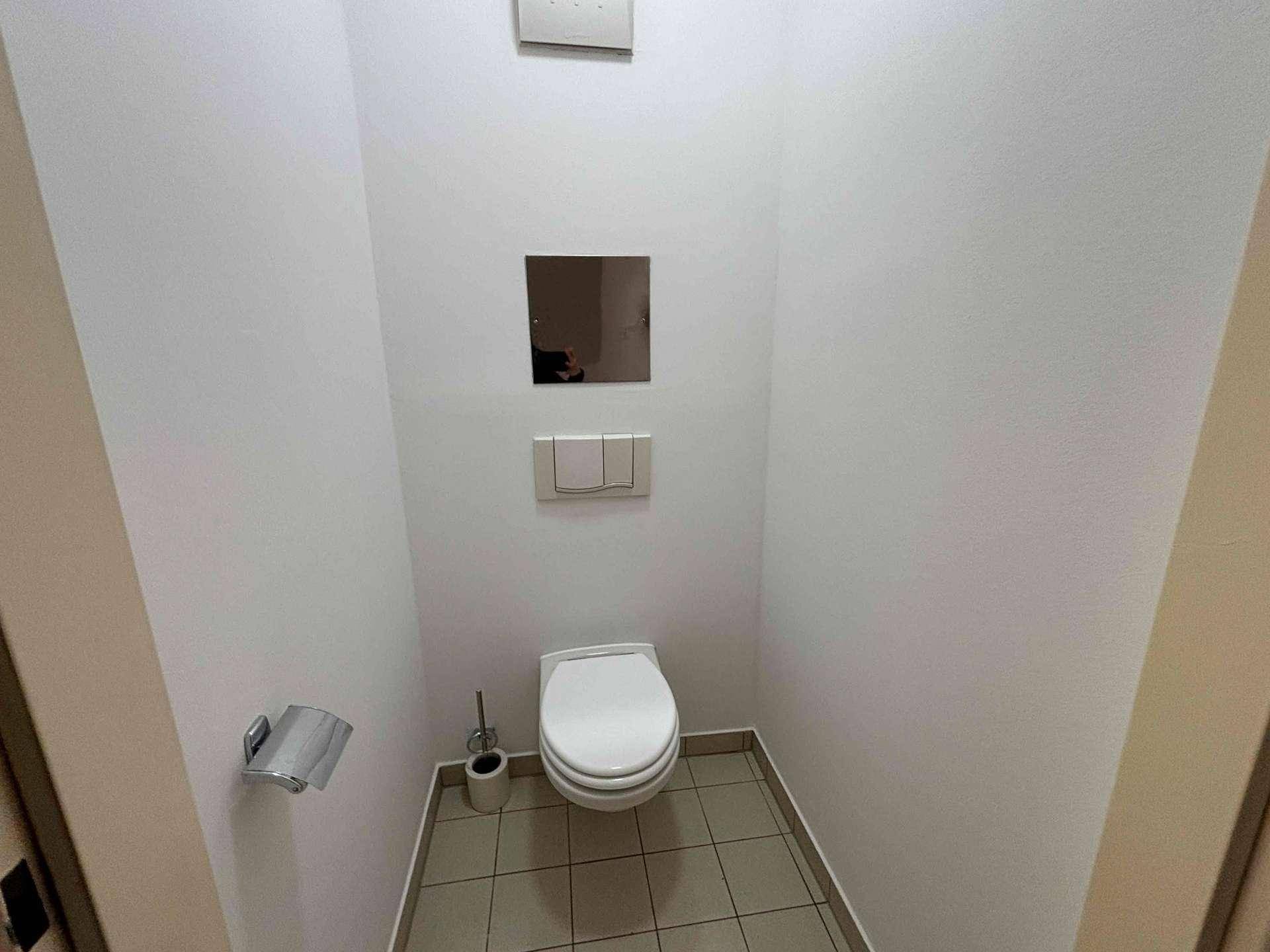 Kleines separates WC mit Toilette, Fliesenboden und einem kleinen Spiegel.