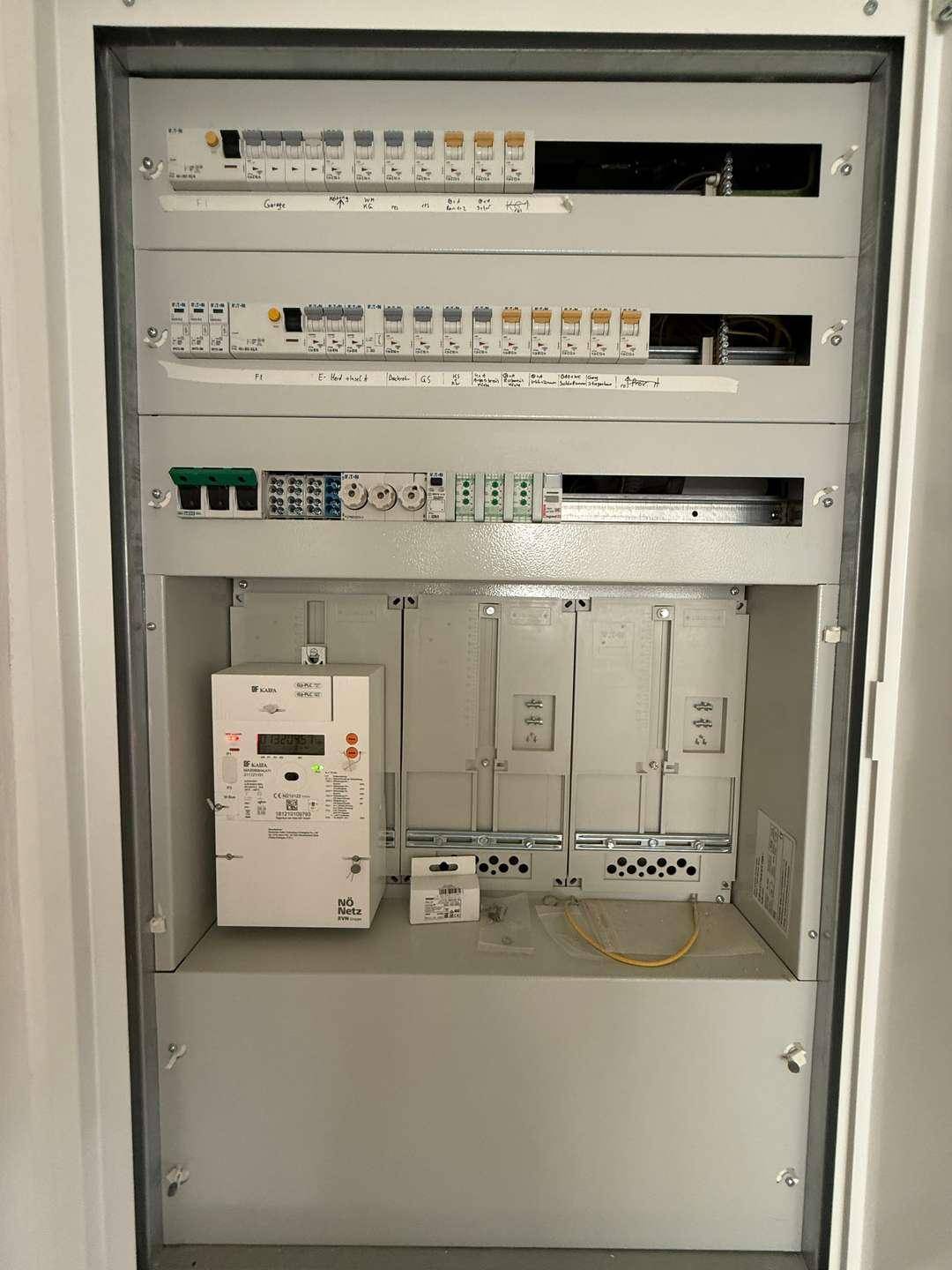 Elektrischer Verteilerkasten und Zähler in einem Technikraum, ordentlich installiert.