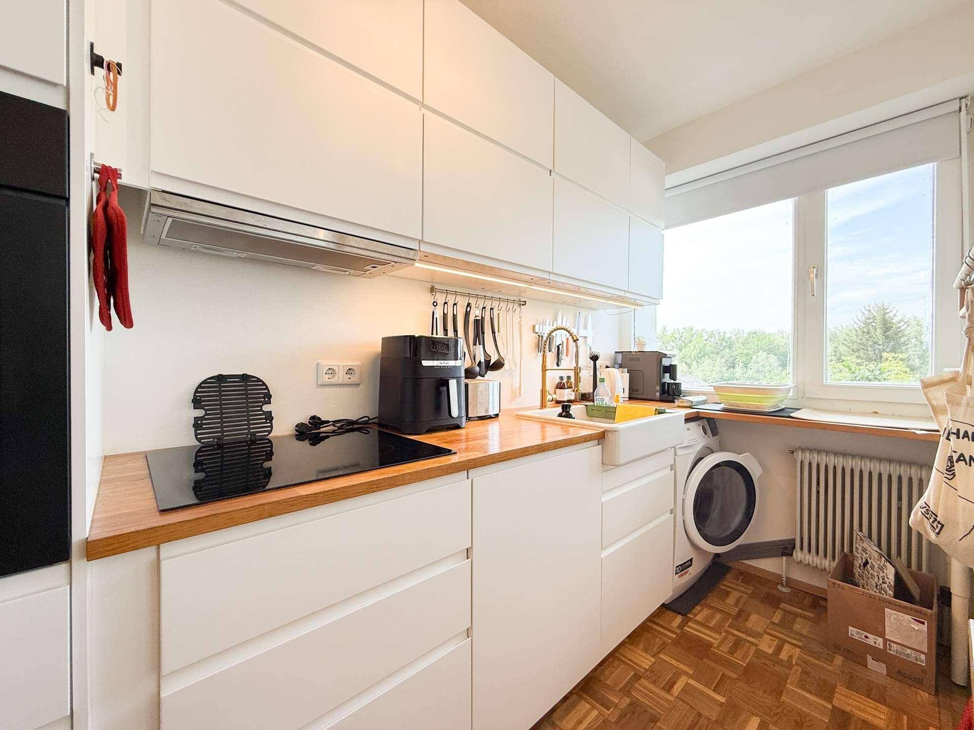 Helle Küche mit Induktionskochfeld, Spülbecken und integrierter Waschmaschine unter dem Fenster.