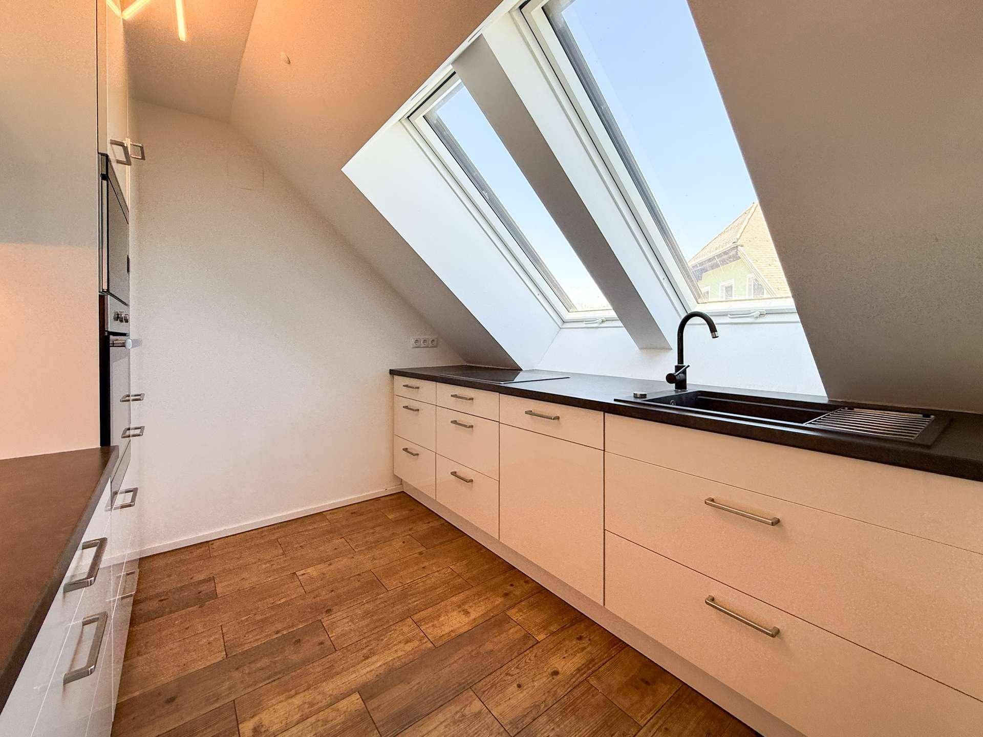 Küchenzeile mit Spülbecken unter einem großen Dachfenster, das viel Tageslicht hereinlässt.