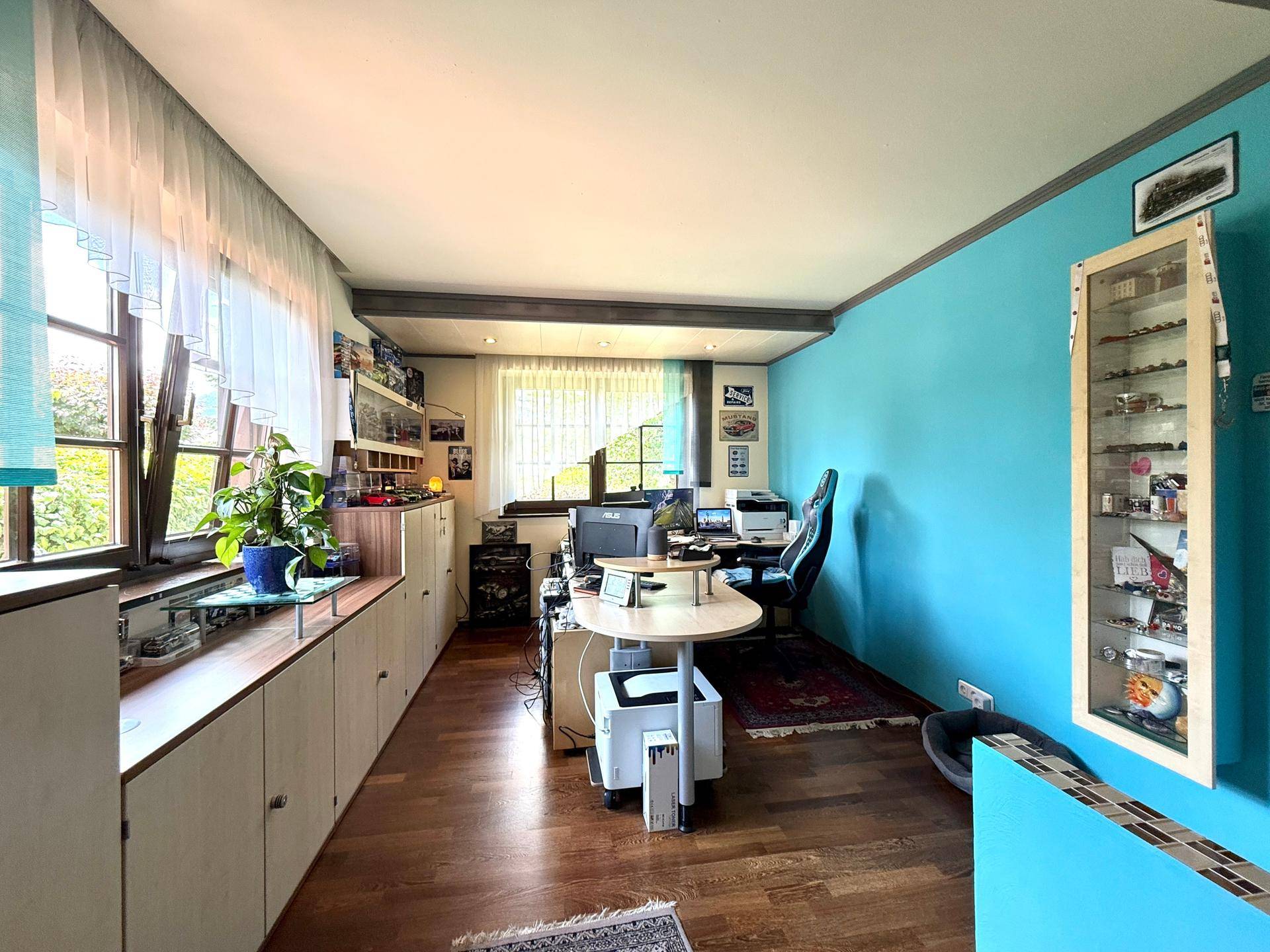 Geräumiges Büro mit langem Schreibtisch, blauer Akzentwand und Holzfußboden.