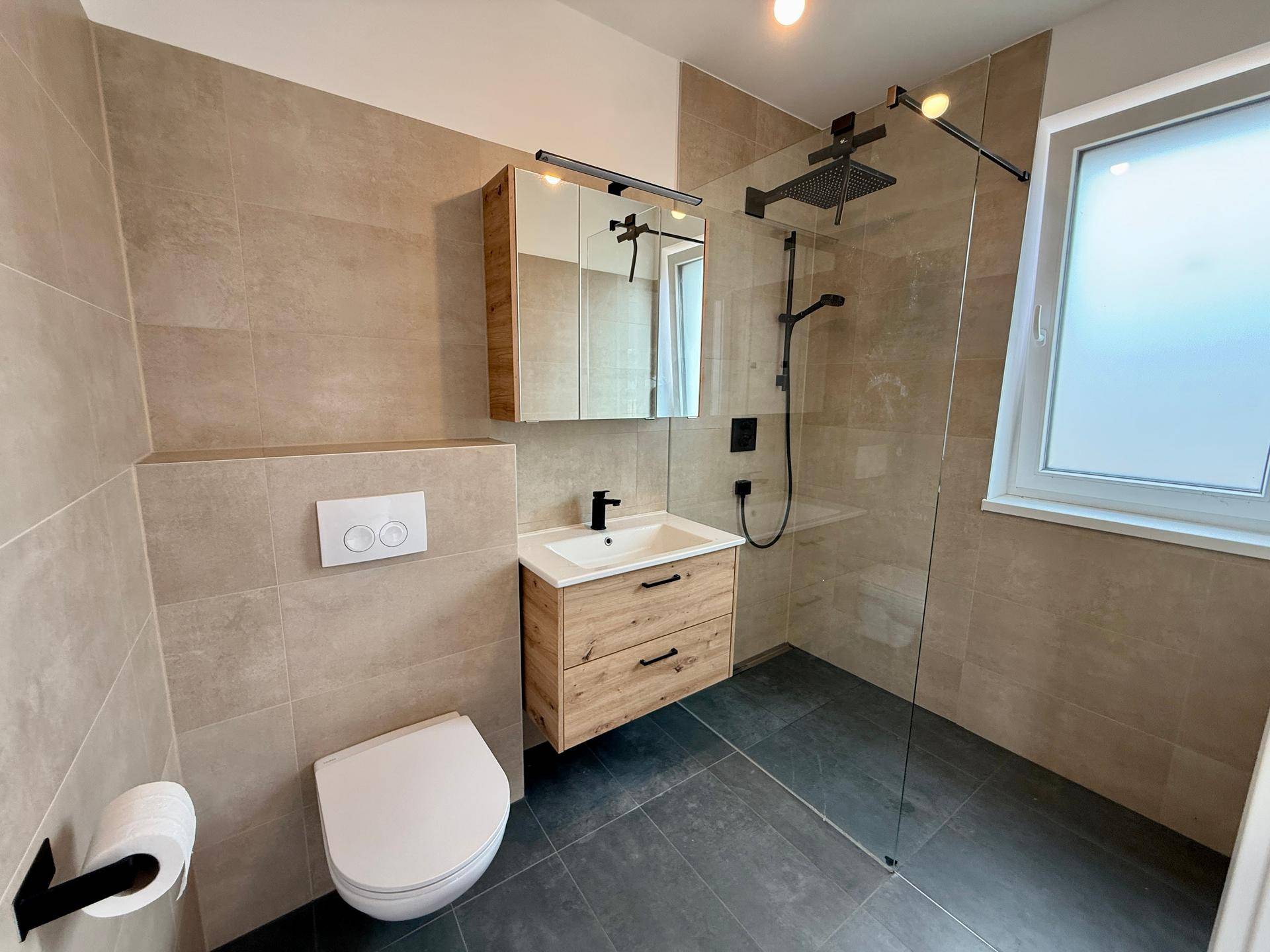 Helles Badezimmer mit begehbarer Dusche, wandhängendem WC, Waschtisch und Fenster.